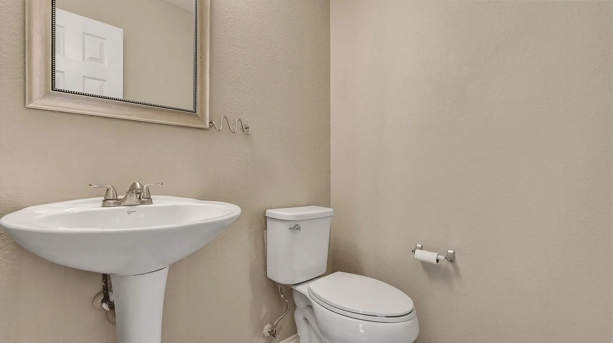 Pedestal sink with brushed nickel faucet, framed mirror, and white toilet