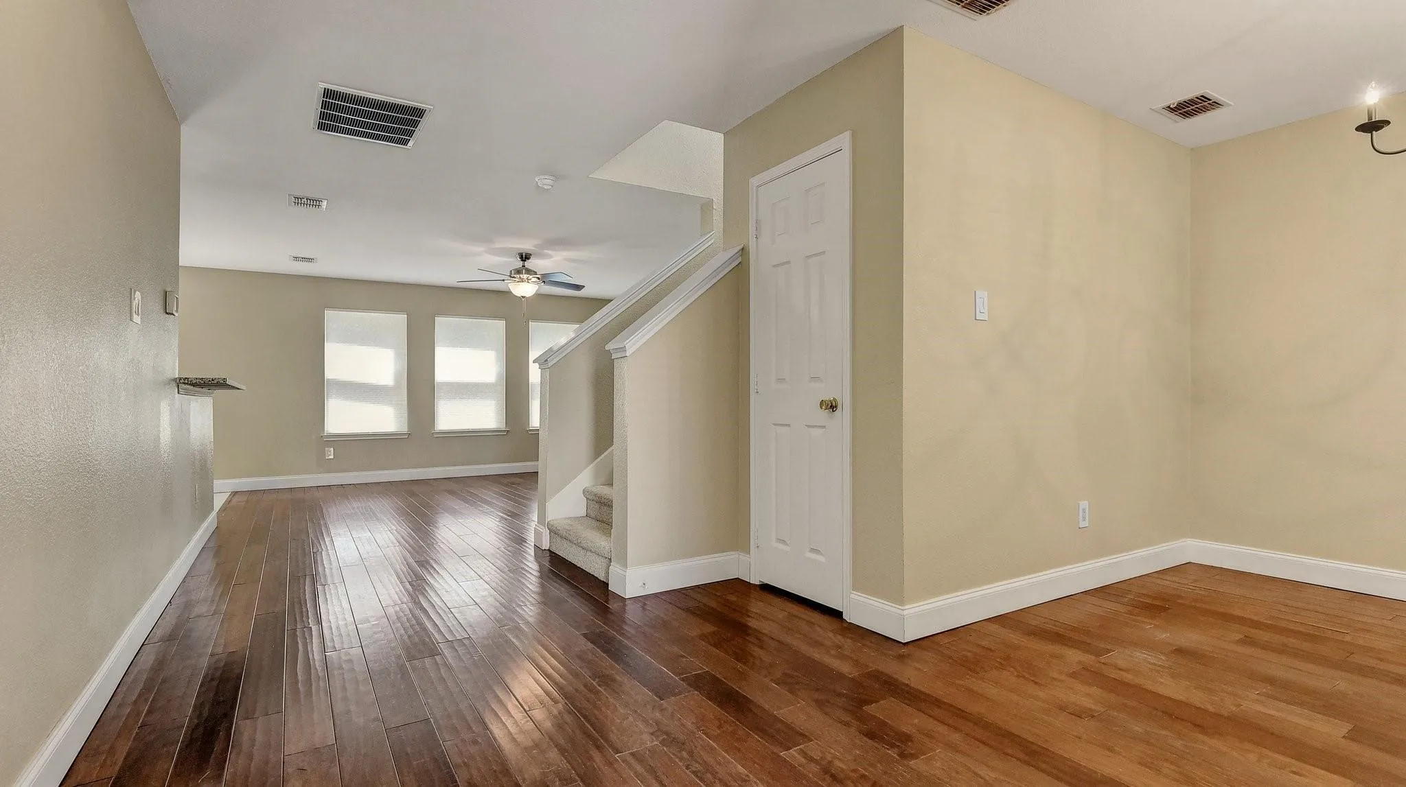 Wood-finish flooring, staircase with carpeted treads, three windows with blinds, ceiling fan, and built-in lighting