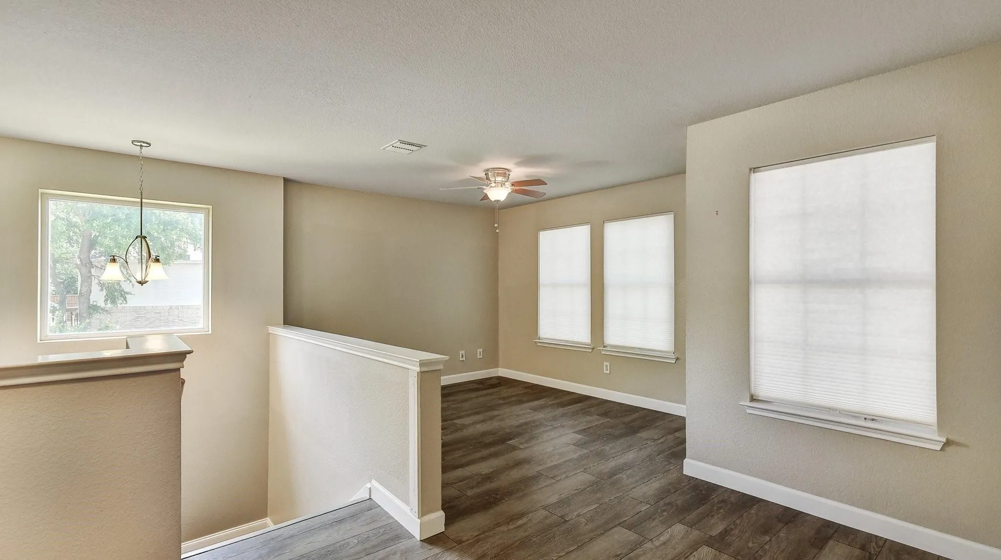 Expansive interior with wood-finish flooring, multiple windows with blinds, a ceiling fan, and a decorative pendant light fixture