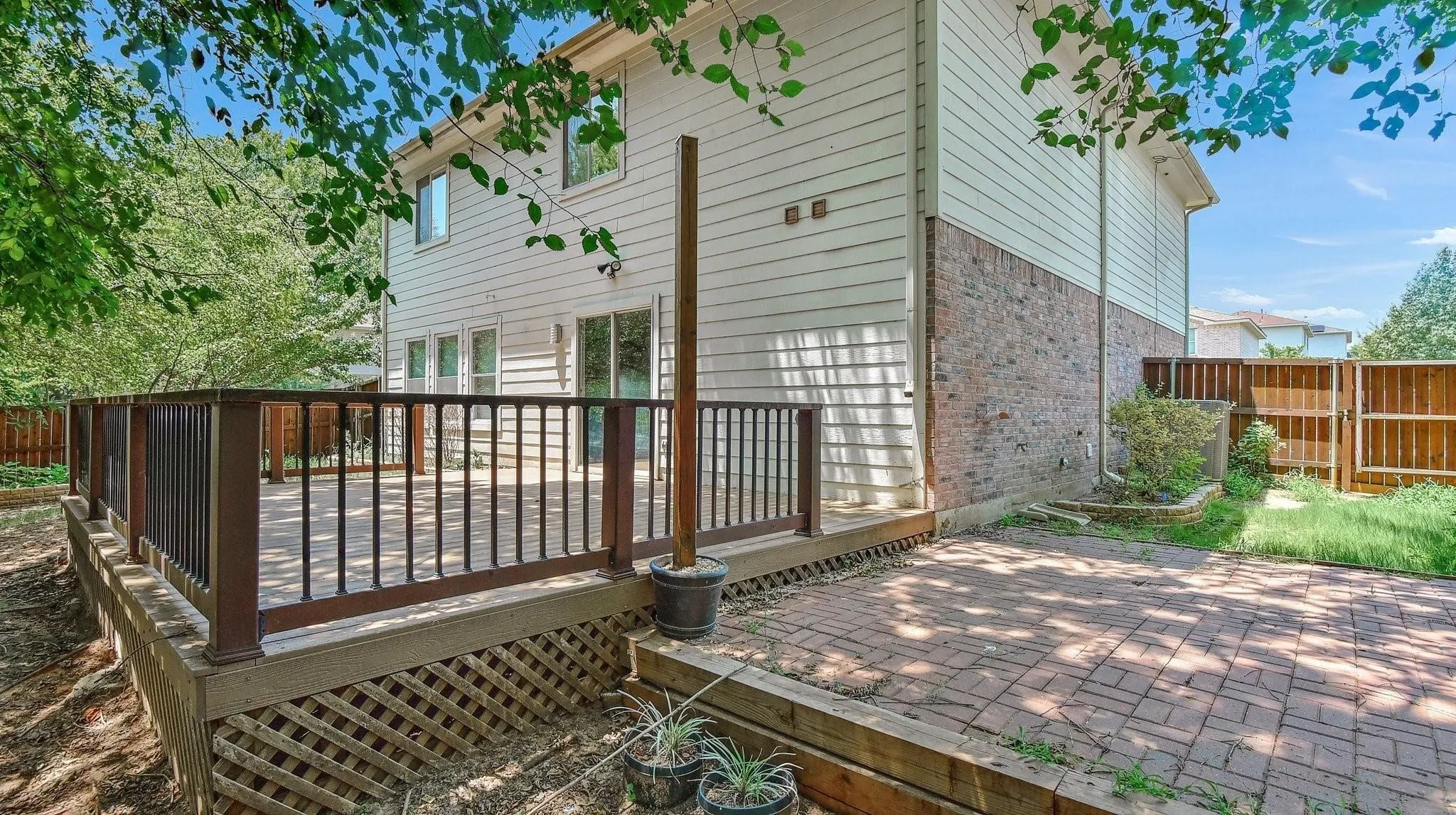 Elevated wood deck with dark railings, siding exterior, brick accent wall, sliding glass doors, and a paver patio