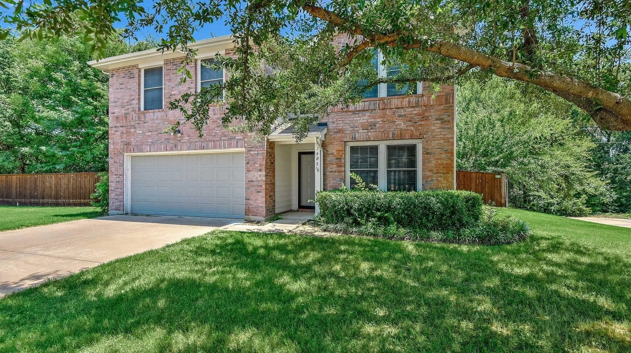 Brick exterior, attached garage, concrete driveway, front yard landscaping, and mature trees