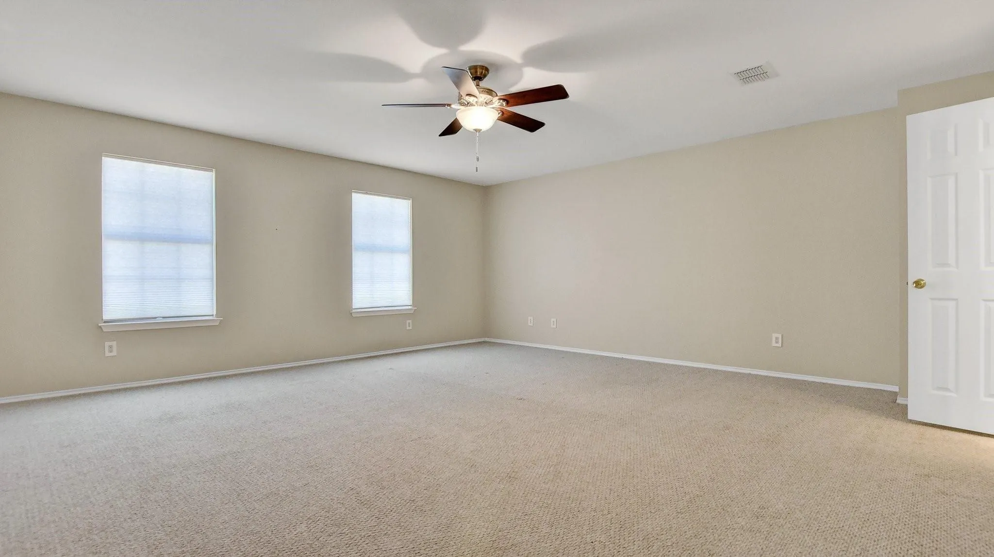 Spacious room featuring neutral carpeting, a ceiling fan with light fixture, and two windows