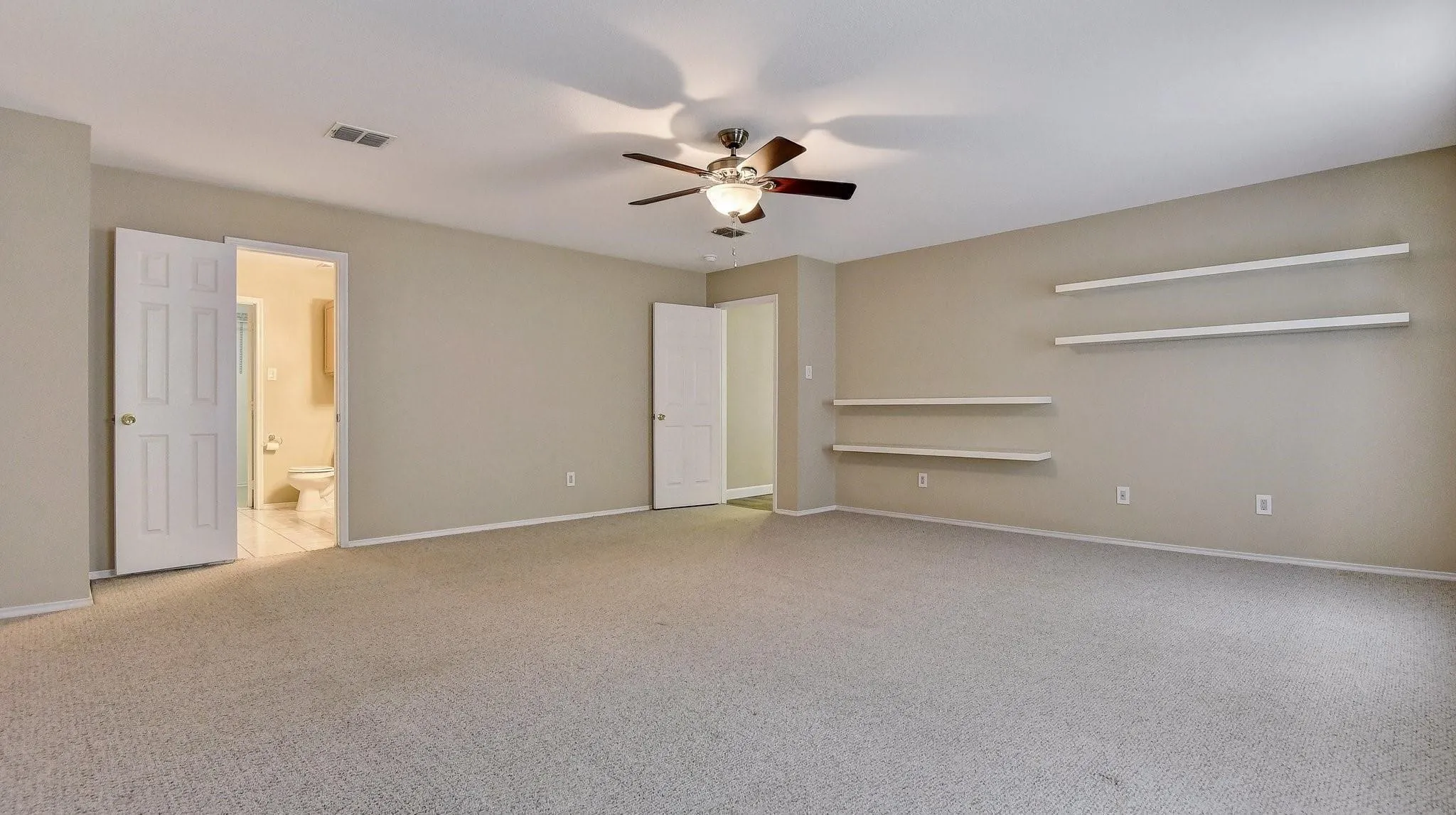 Expansive room featuring neutral-toned carpet flooring, a ceiling fan, and built-in wall shelving