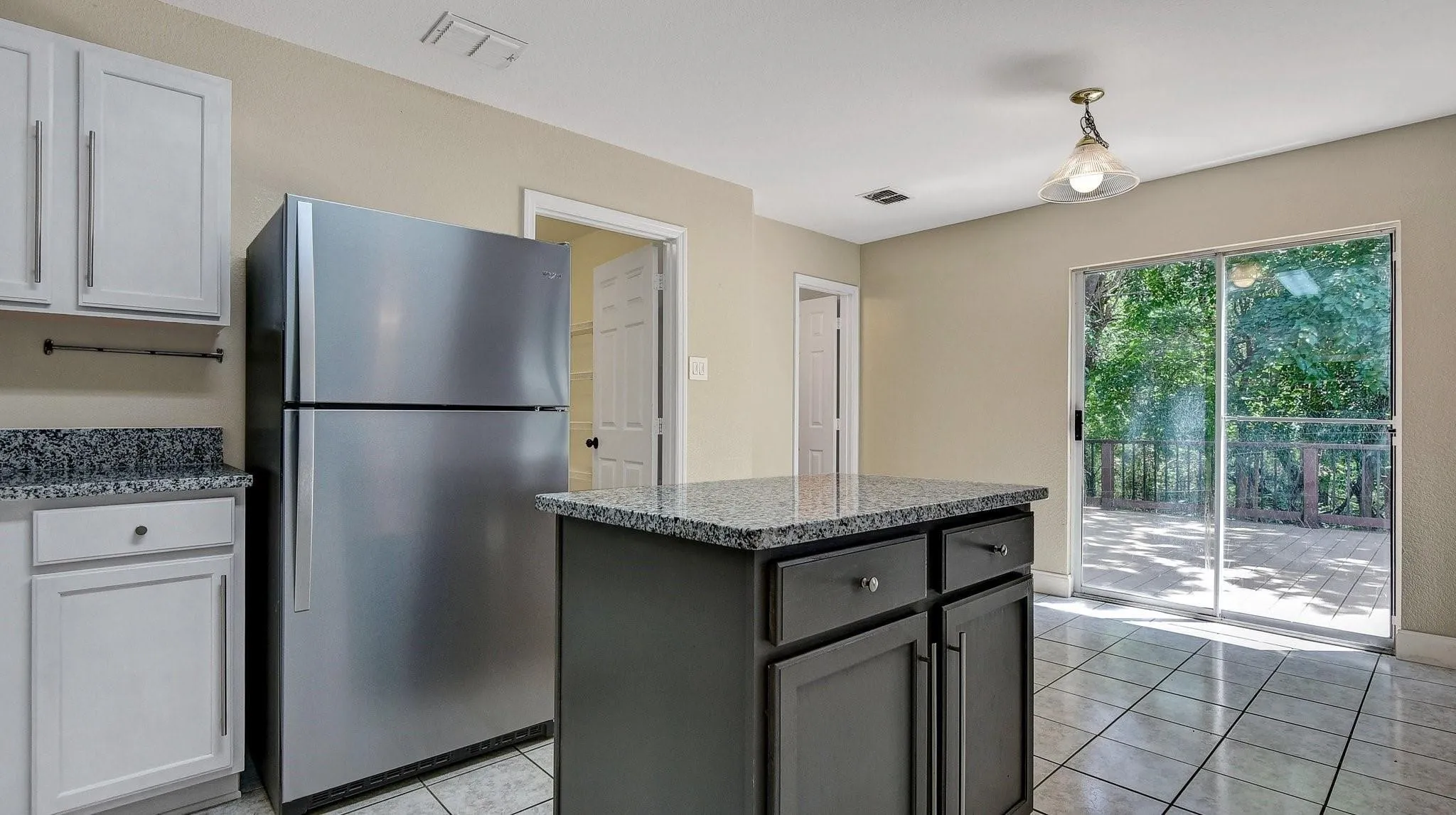 Kitchen featuring an island with stone countertop, white cabinetry with matching stone countertops, stainless steel refrigerator, and tile flooring