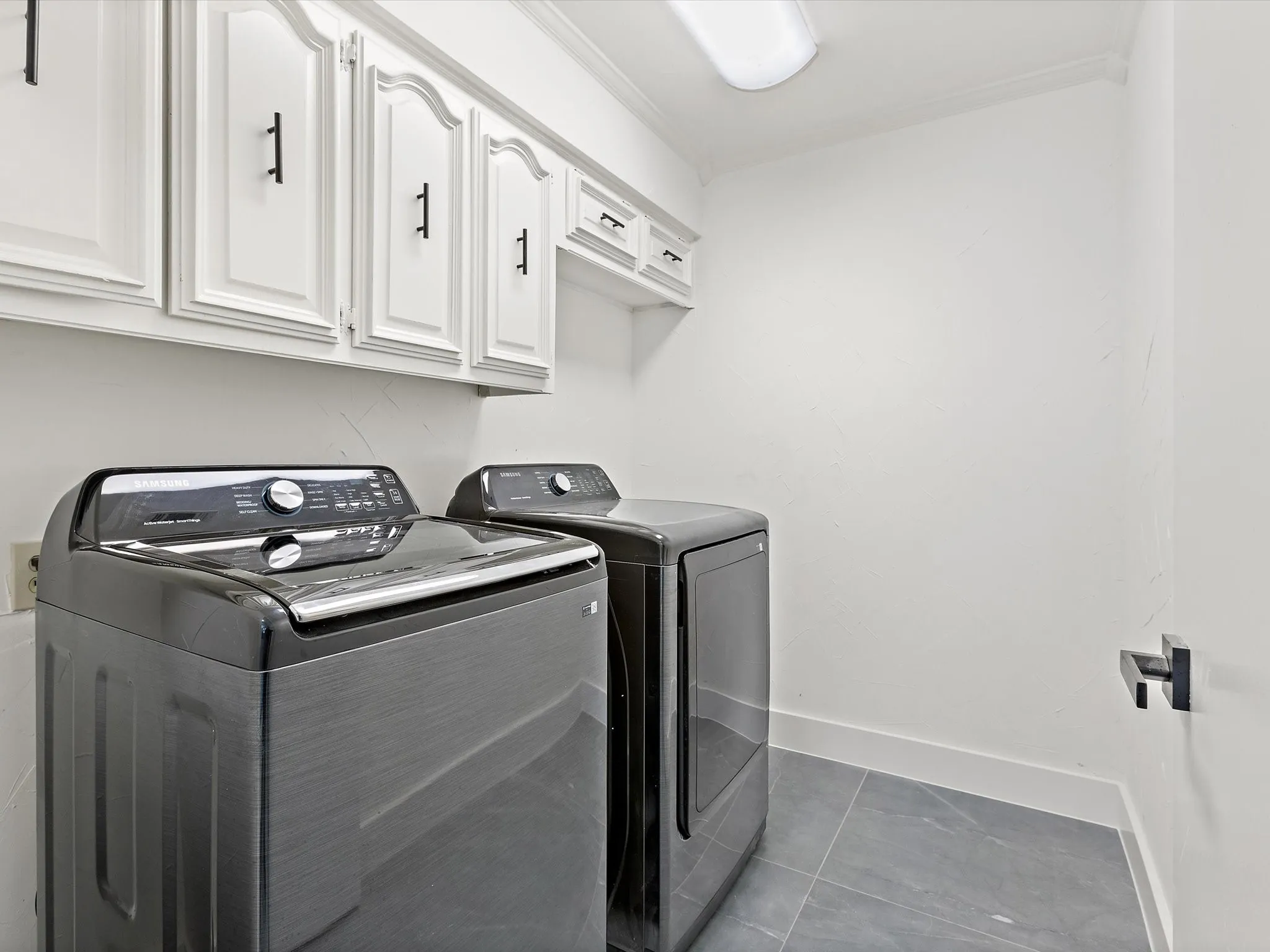 Laundry area with separate washer and dryer, cabinet space, light tile patterned floors, and ornamental molding