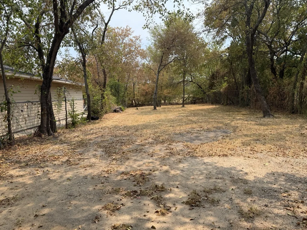 Expansive lot featuring mature trees and a partial chain-link fence