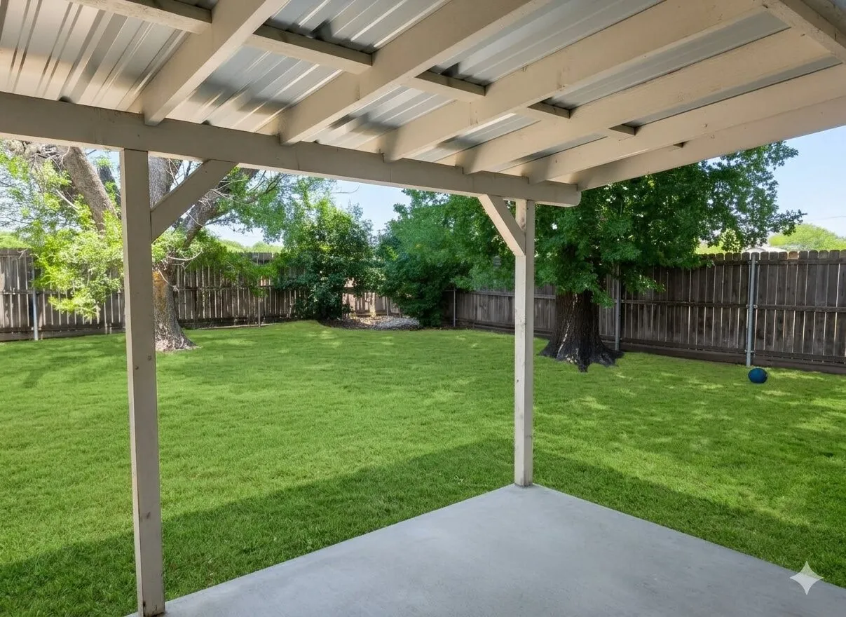 Covered patio with a concrete surface, expansive lawn, mature perimeter trees, and a wood privacy fence