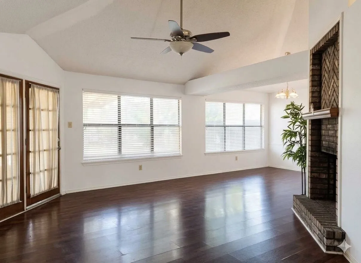 Vaulted ceiling, wood-finish flooring, brick fireplace, multiple windows, and a ceiling fan