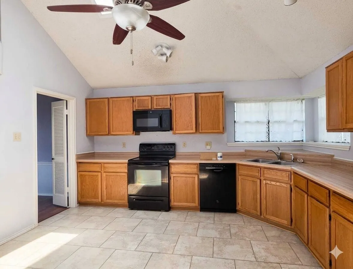 Vaulted ceiling with ceiling fan, tile flooring, wood-finish cabinetry, black appliances, and a bay window