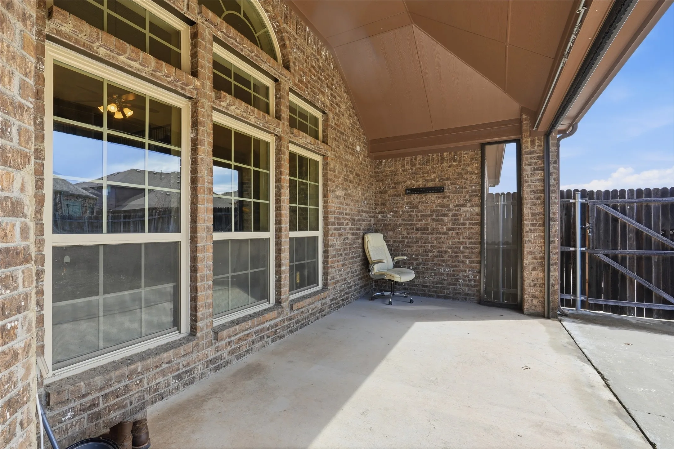 Covered concrete patio featuring a brick exterior wall, multiple windows with arched transom, and a solid wood fence