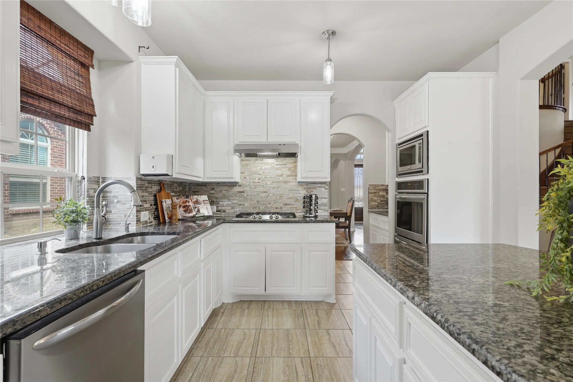 White cabinetry with dark stone countertops, stainless steel appliances, a tile backsplash, and wood-finish flooring