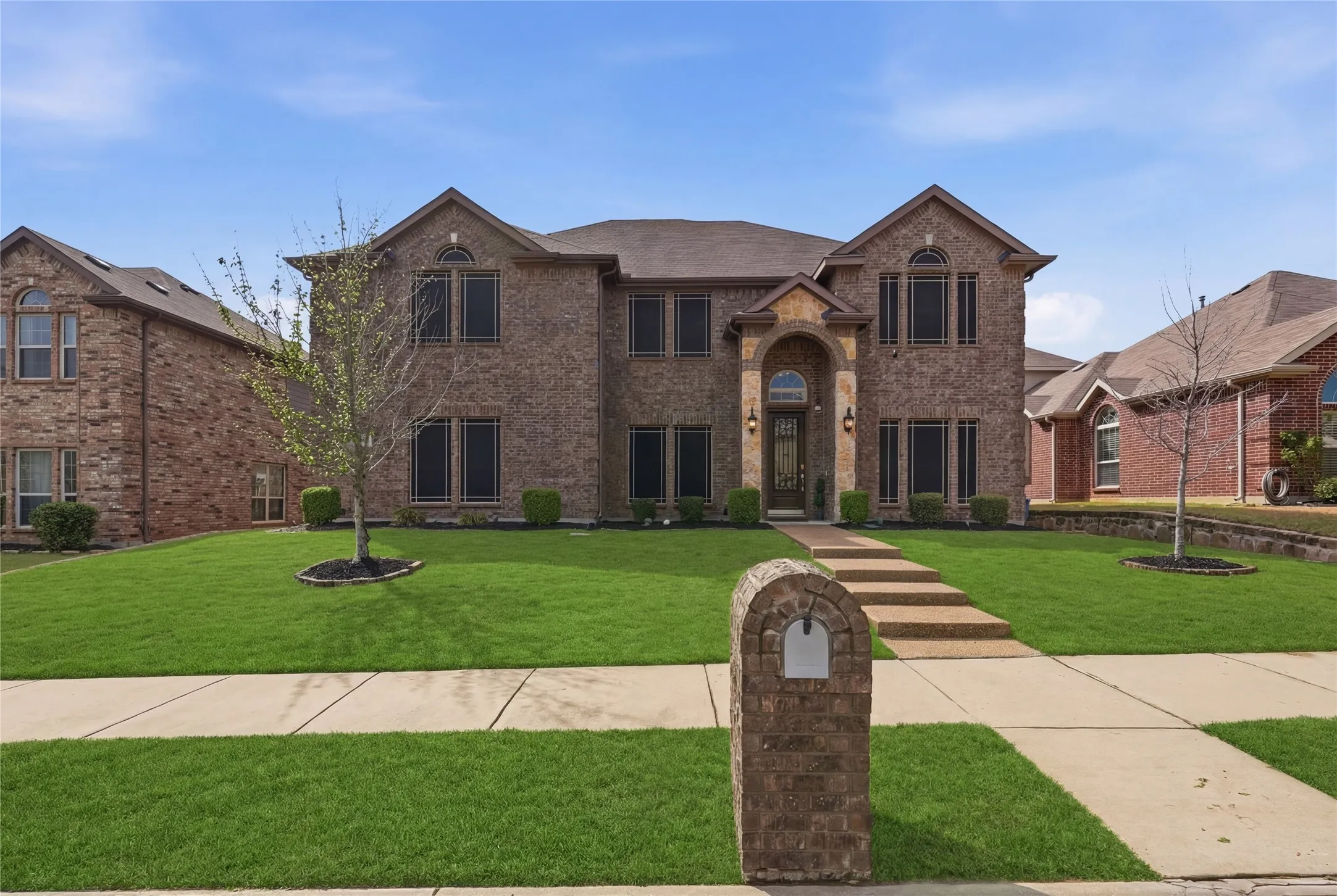 Two-story brick exterior with arched entry, gabled rooflines, stone-clad entryway, and mature landscaping