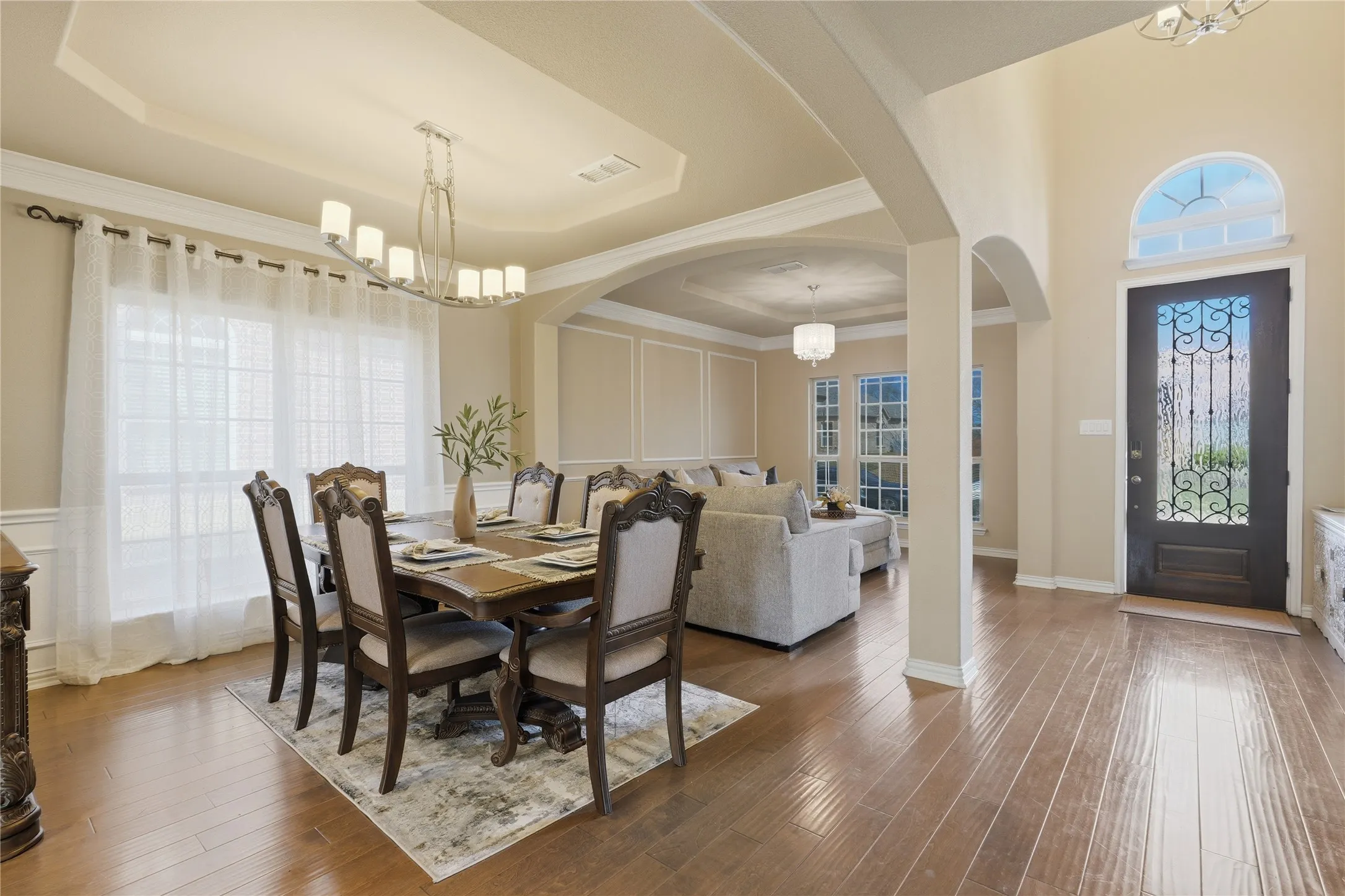 Wood-finish flooring throughout, decorative arched doorways, tray ceiling with crown molding, and a detailed front entry door with an arched transom
