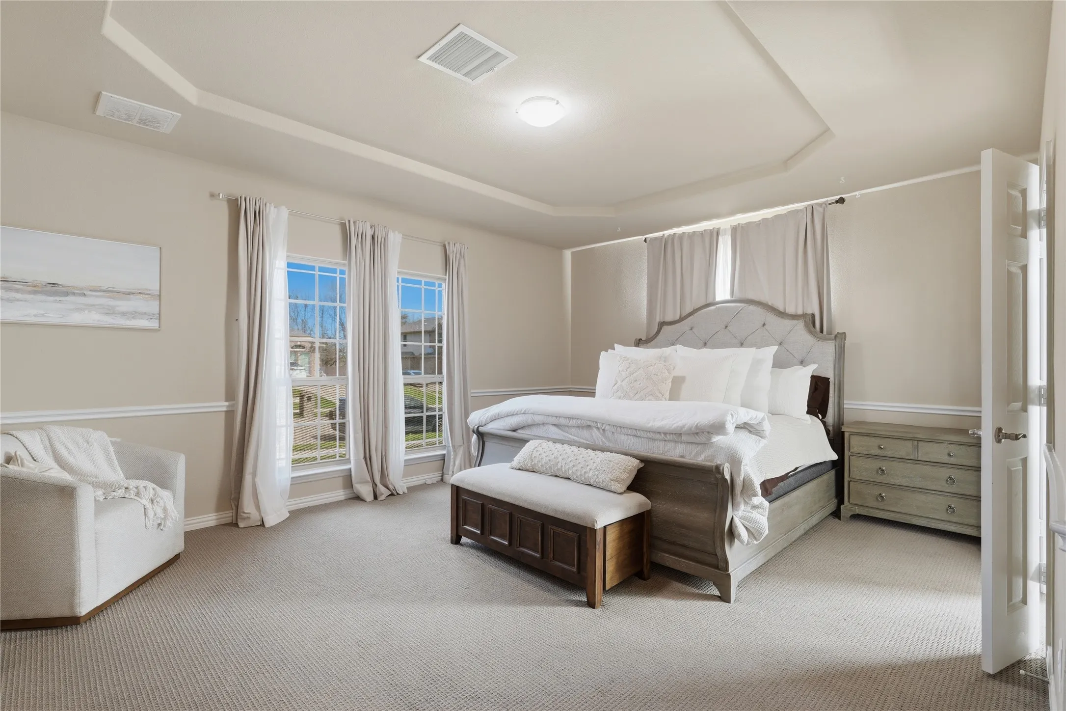 Recessed ceiling with an overhead light fixture, two double-hung windows, light-toned carpeting, and a paneled door