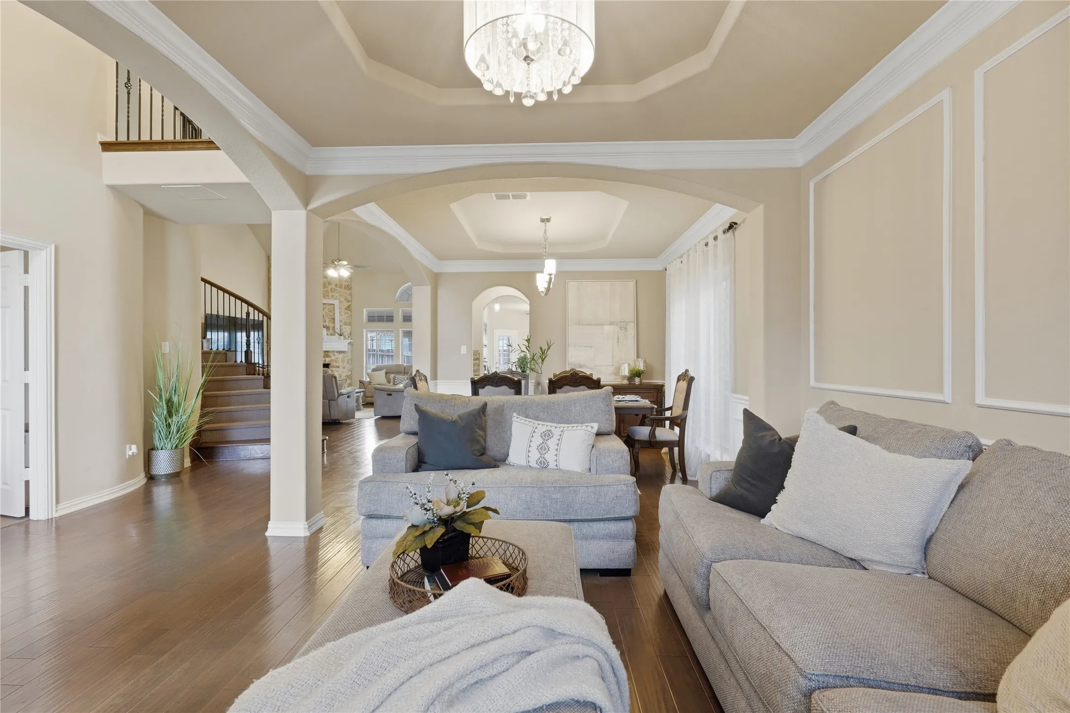 Wood-finish flooring throughout, decorative wall molding, arched doorways, tray ceiling, and a prominent staircase with dark wood railings