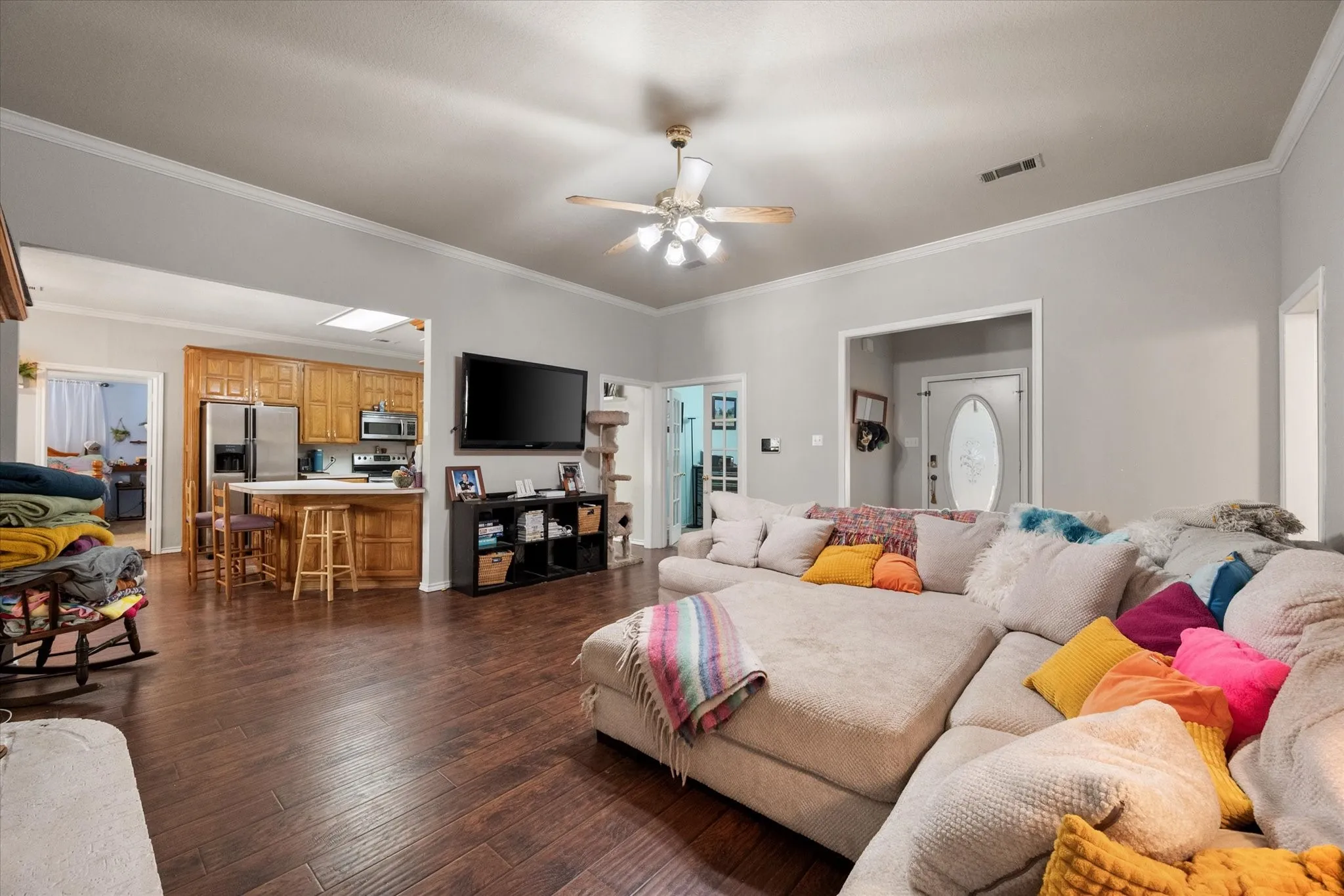 Wood-finish flooring throughout, crown molding, ceiling fan with light fixture, recessed lighting, and kitchen with wood cabinetry