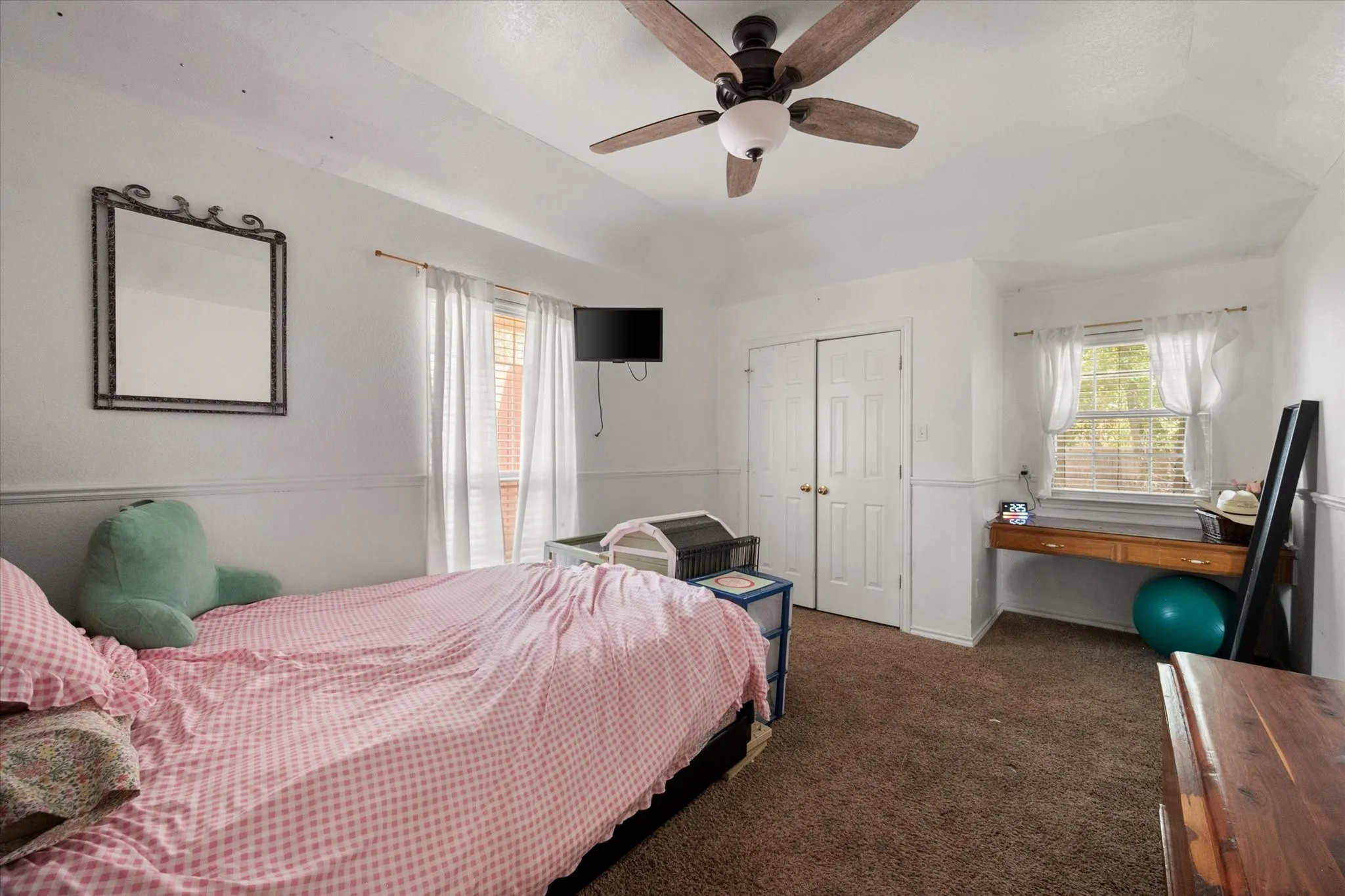 Sloped ceiling with a ceiling fan light fixture, white walls with wainscoting, and a window with blinds