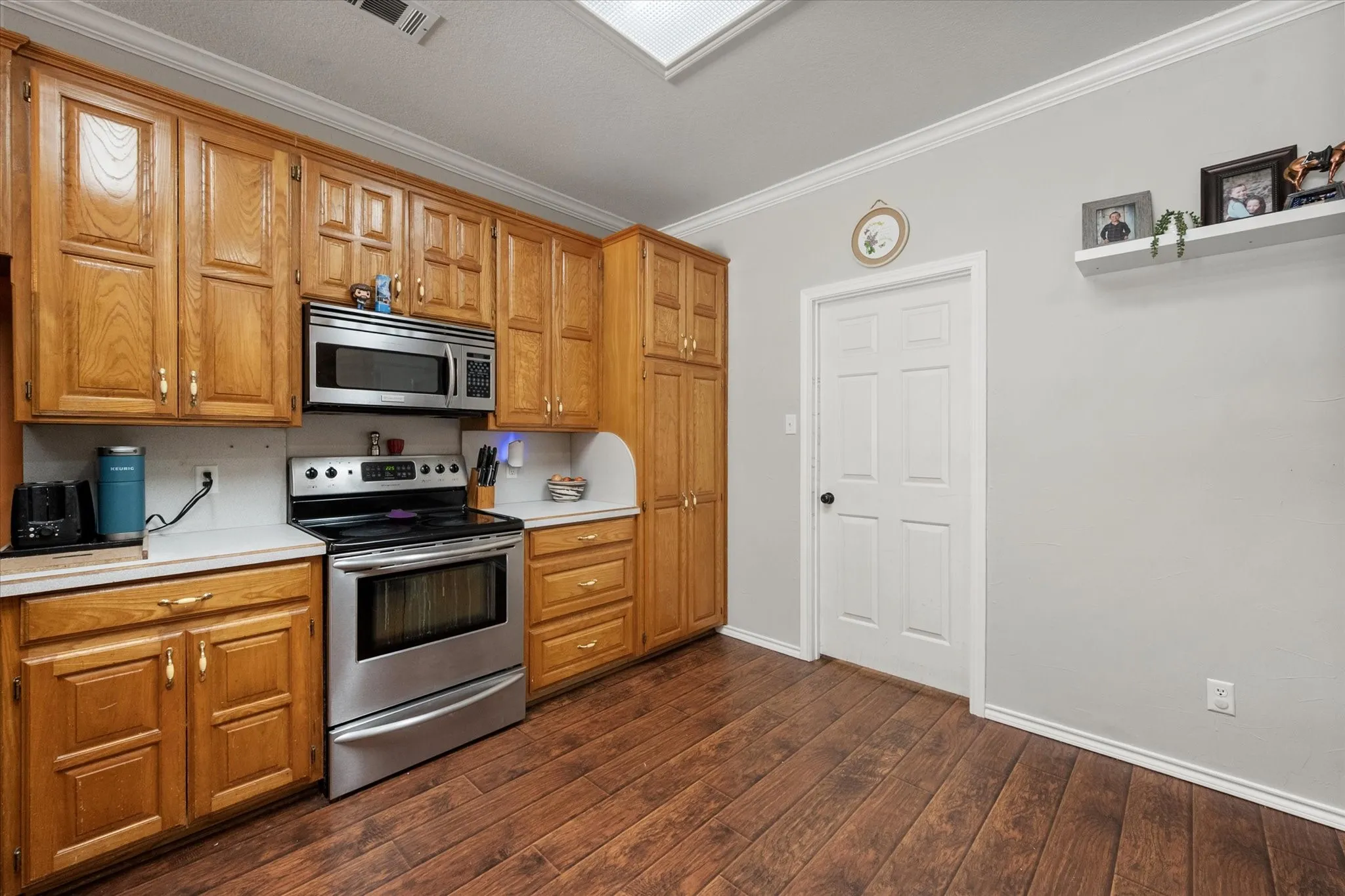 Wood-finish flooring, wood cabinetry, stainless steel range, built-in microwave, and crown molding