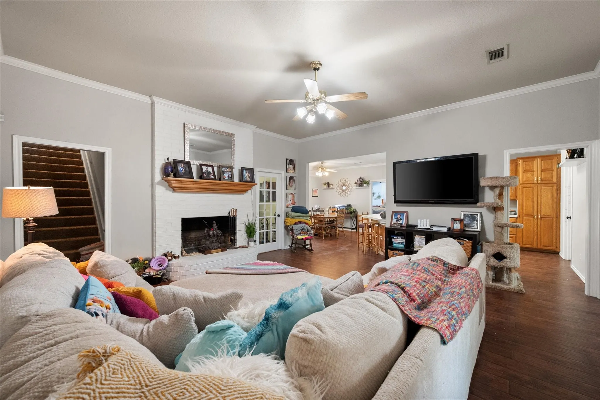 Spacious living area featuring wood-finish flooring, a white brick fireplace with a wood mantle, and a ceiling fan