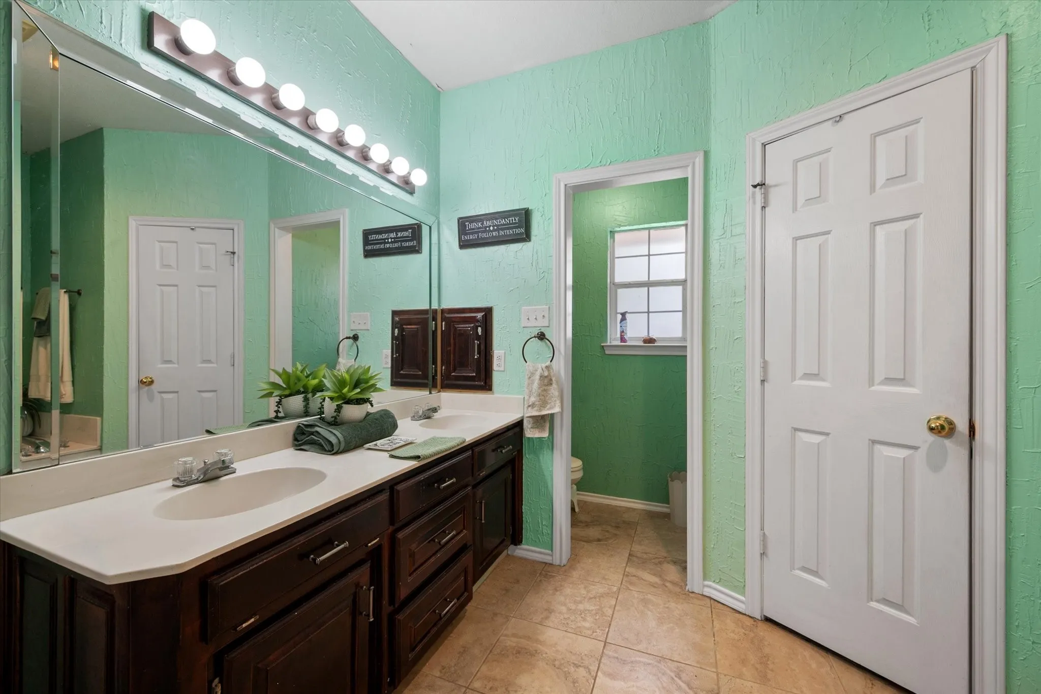 Dual vanity with integrated sinks, expansive wall mirror, dark wood-finish cabinetry, and overhead bar lighting