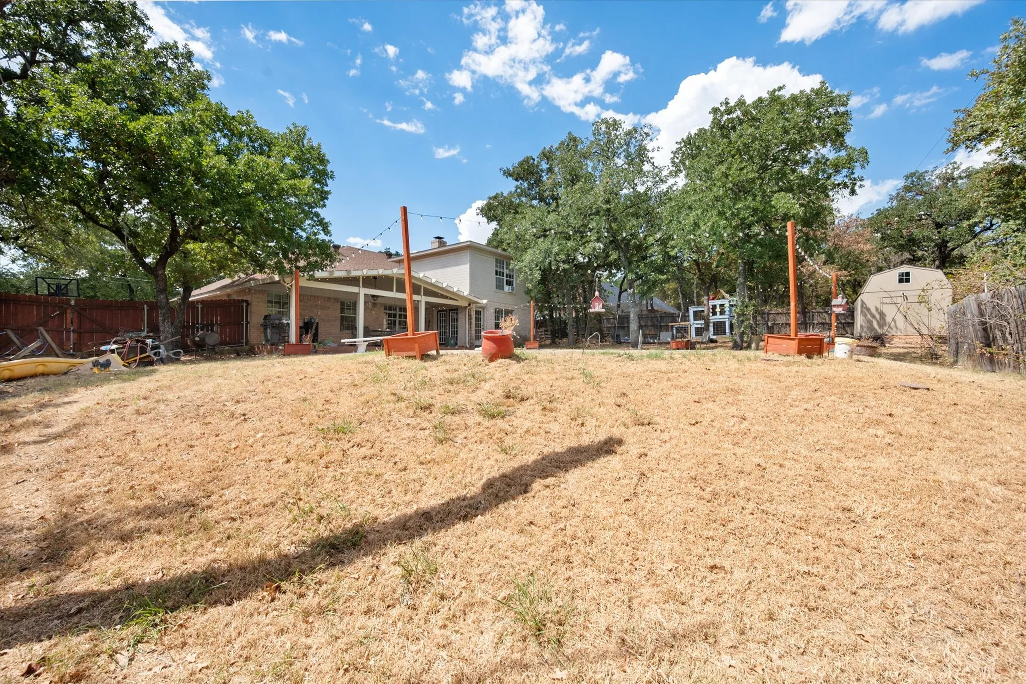 Expansive backyard with a covered patio, mature trees, and a storage shed