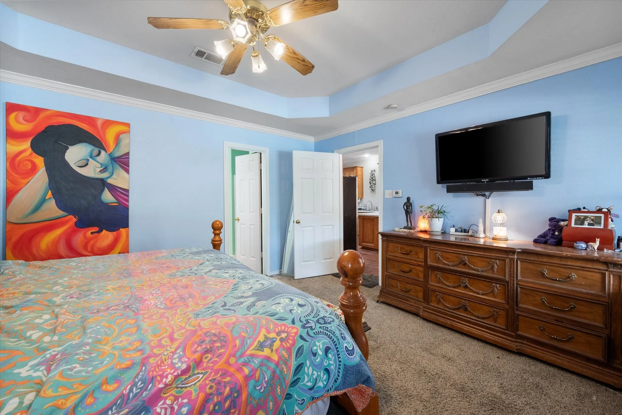 Tray ceiling with crown molding, wall-mounted television, and ceiling fan with lighting