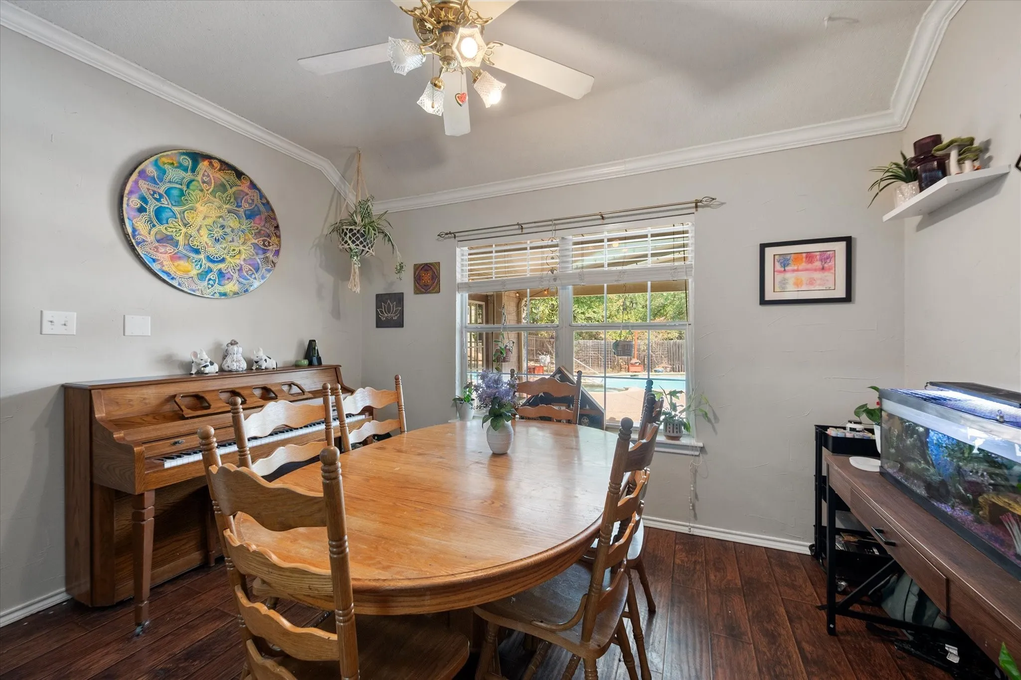 Wood-finish flooring, crown molding, and a ceiling fan are featured in this room with a large window overlooking the outdoor pool
