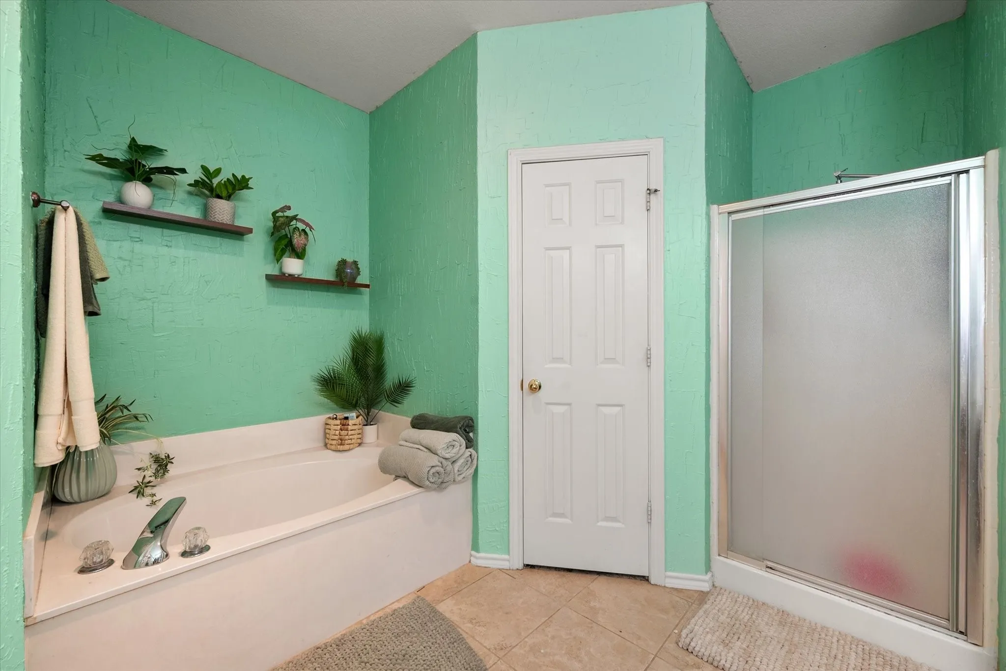 Built-in soaking tub, separate shower enclosure with frosted glass, ceramic tile flooring, and integrated wall shelving