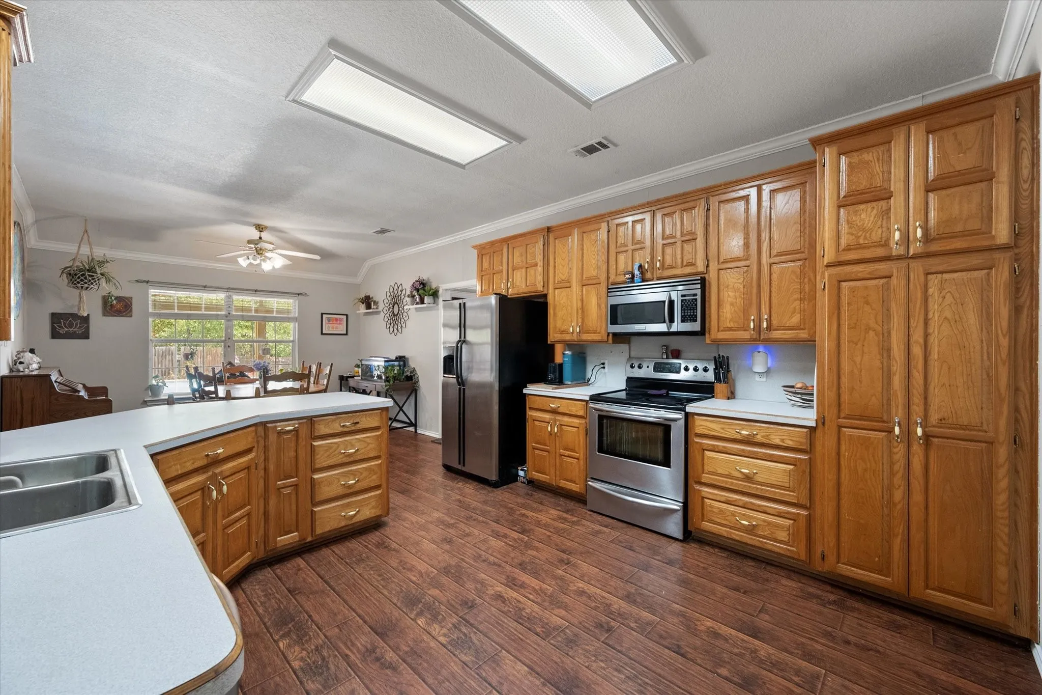 Wood-finish flooring throughout, extensive cabinetry with brass hardware, stainless steel appliances, a double basin sink, and recessed lighting