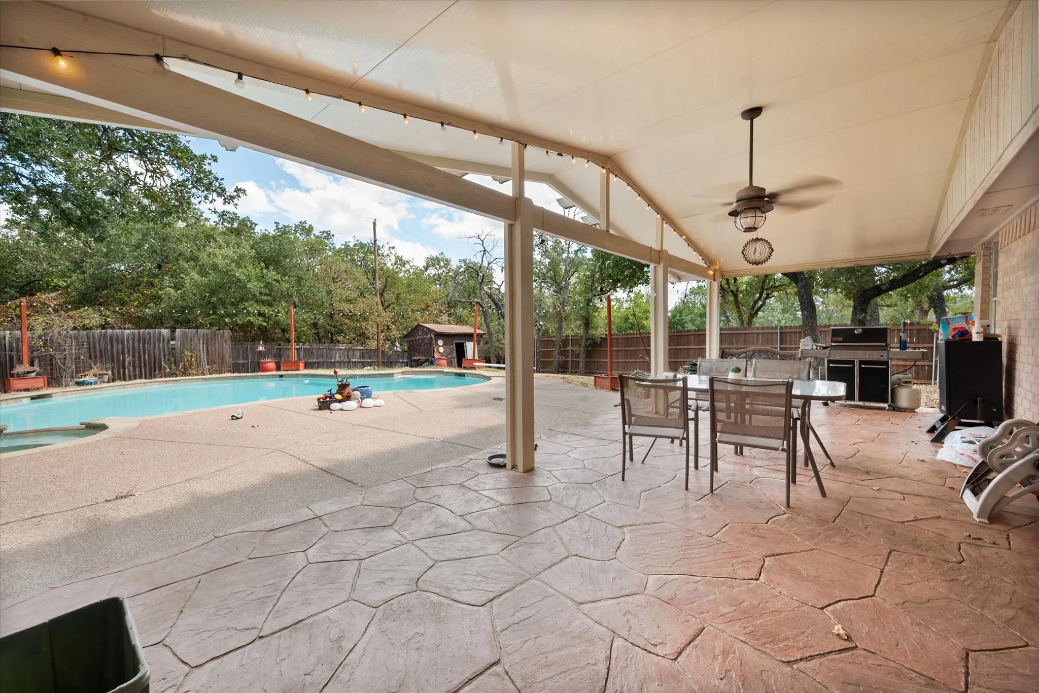 Expansive covered patio featuring two-tone stamped concrete flooring, a ceiling fan, and string lighting