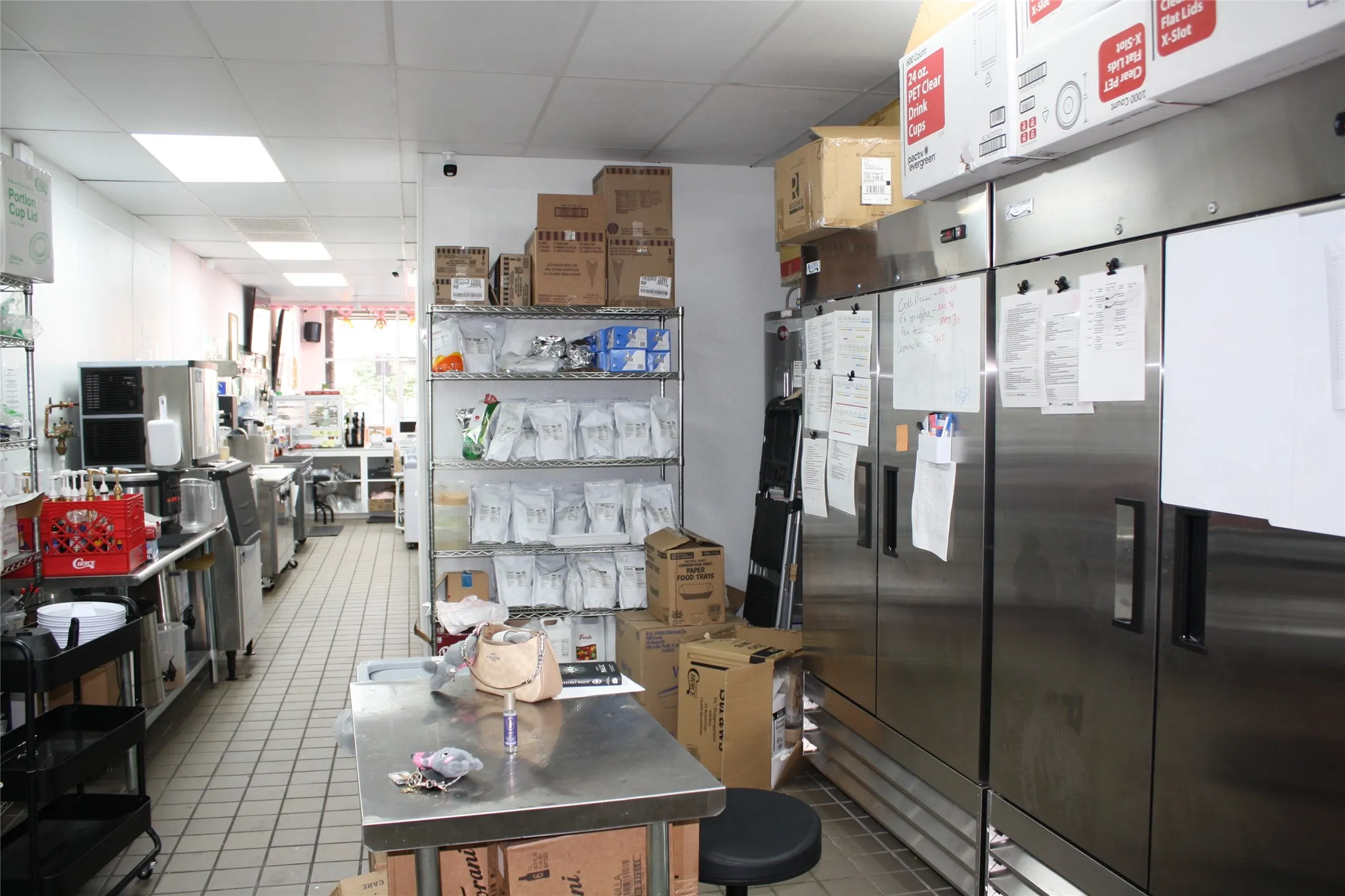Commercial kitchen space featuring multiple stainless steel refrigeration units, stainless steel work surfaces, grid tile flooring, and track lighting