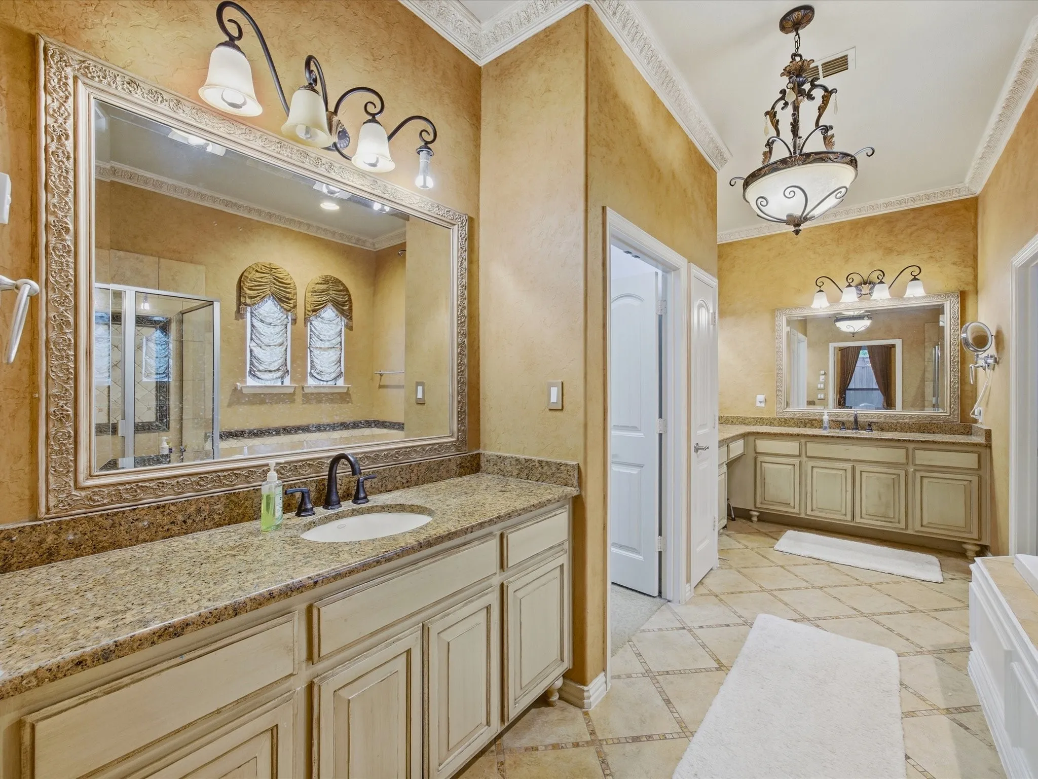 Dual vanities with granite countertops, tile flooring, ornate chandelier, and custom window treatments