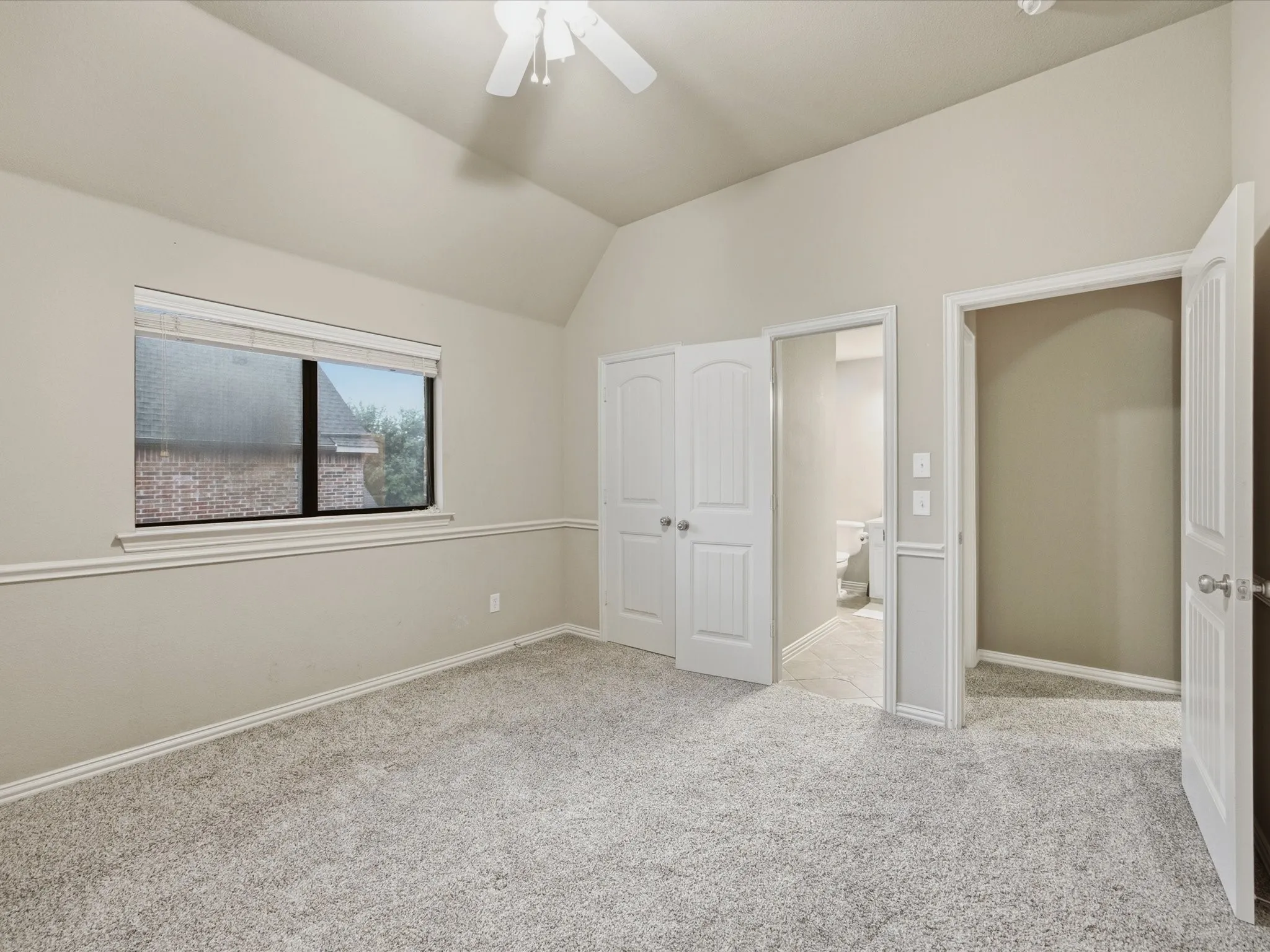Vaulted ceiling with ceiling fan, light-toned carpeting, window with blinds, white trim, and interior doors