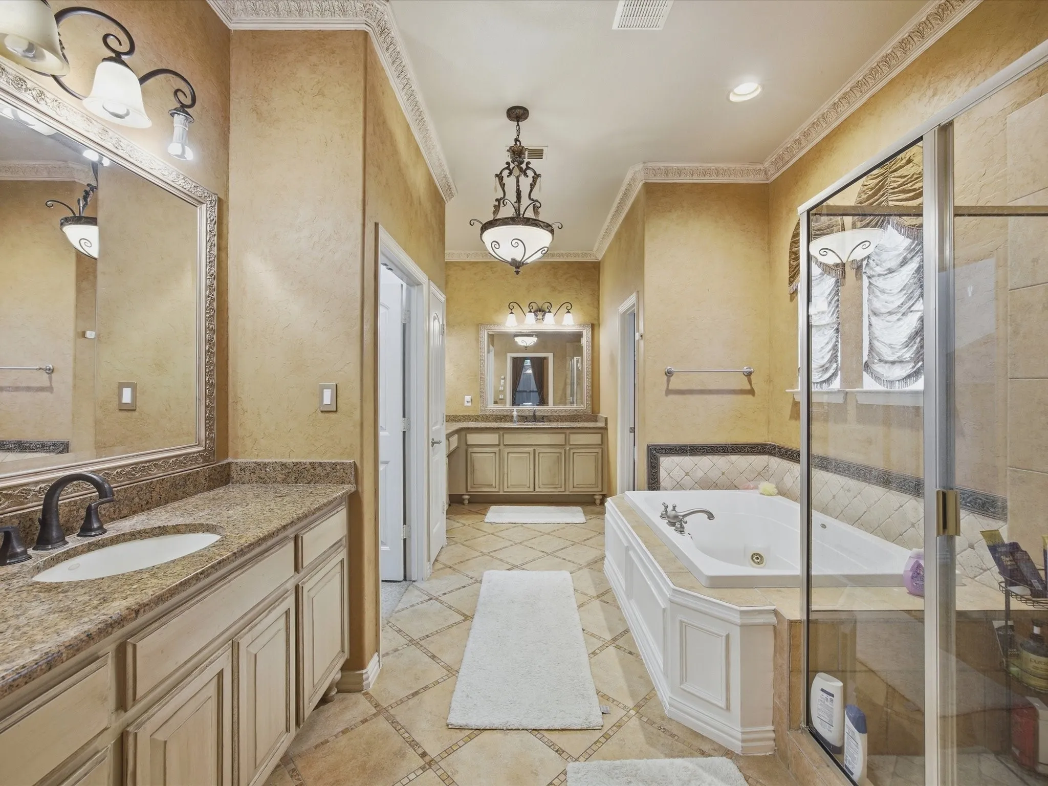 Dual vanity sinks with granite countertops, a built-in jetted tub, separate glass-enclosed shower, and decorative crown molding