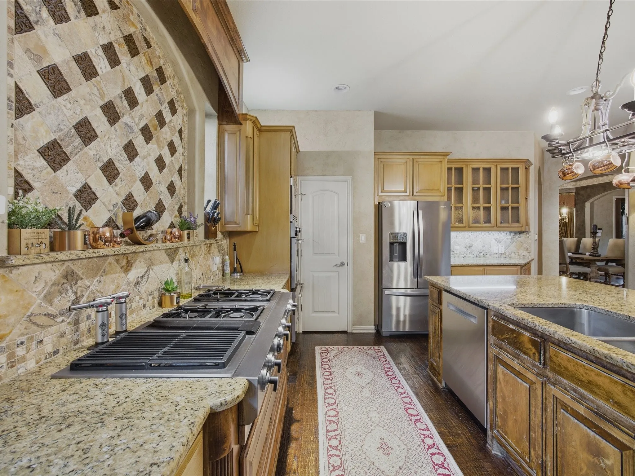 Stainless steel professional-grade cooktop with griddle, granite countertops, wood-finish cabinetry, stainless steel refrigerator, and built-in dishwasher