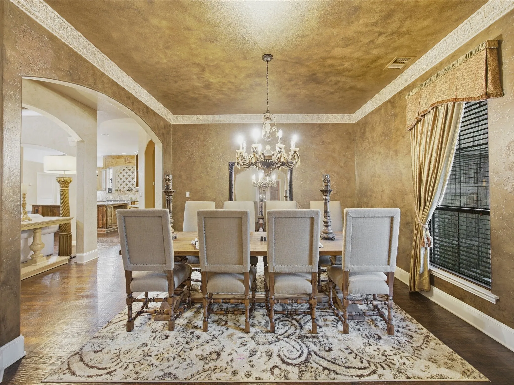 Ornate chandelier, decorative ceiling treatment, wood-finish flooring, cased archways, and a single window with blinds