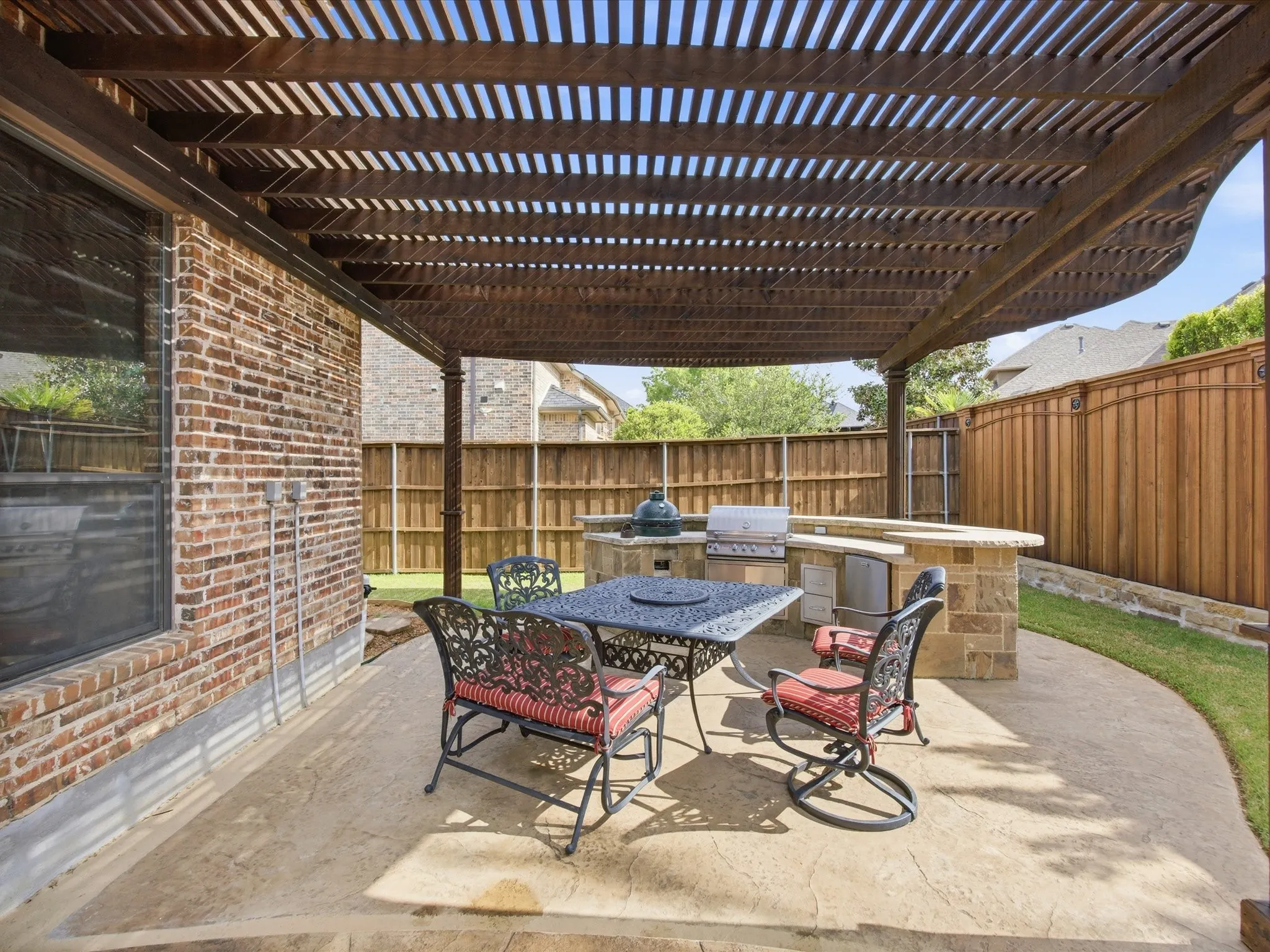 Expansive outdoor living area featuring a decorative wood pergola, stamped concrete patio, and a built-in stone and countertop outdoor kitchen