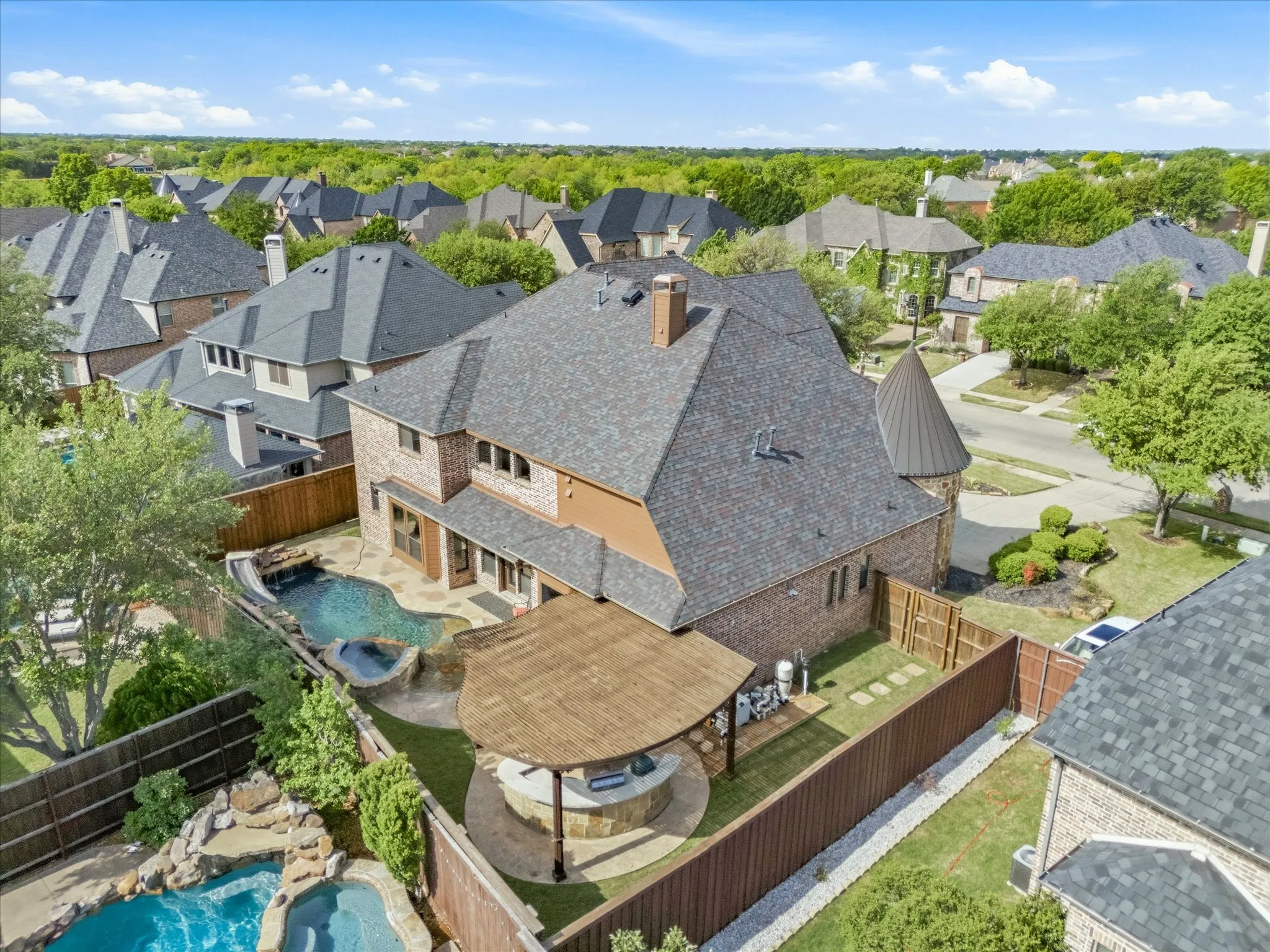 Brick exterior with a conical turret, two swimming pools with rock features, a hot tub, and a covered outdoor living area