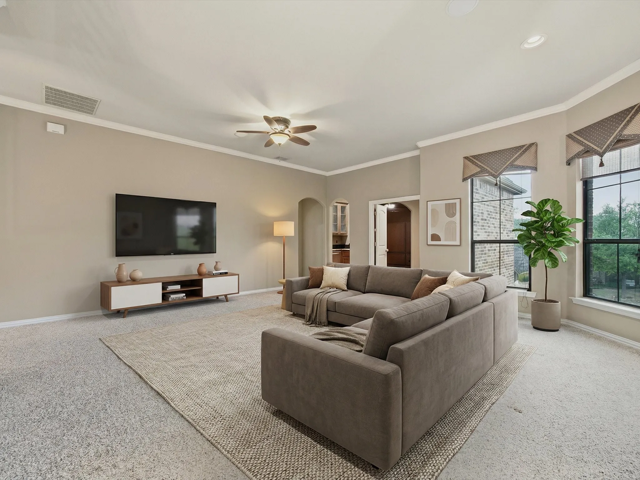 Recessed lighting illuminates a spacious room featuring a ceiling fan, crown molding, and large windows