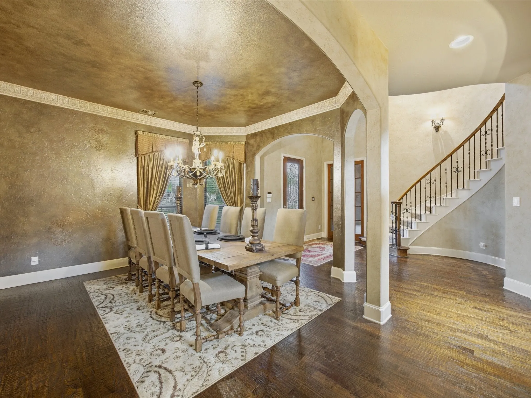 Hardwood flooring throughout, decorative wall finish, crown molding, arched entryways, and a curved staircase with wrought iron balusters