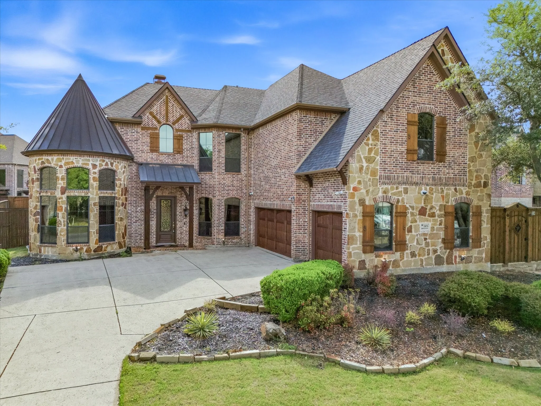 Brick and stone exterior with decorative wood shutters, a conical turret, and an attached two-car garage