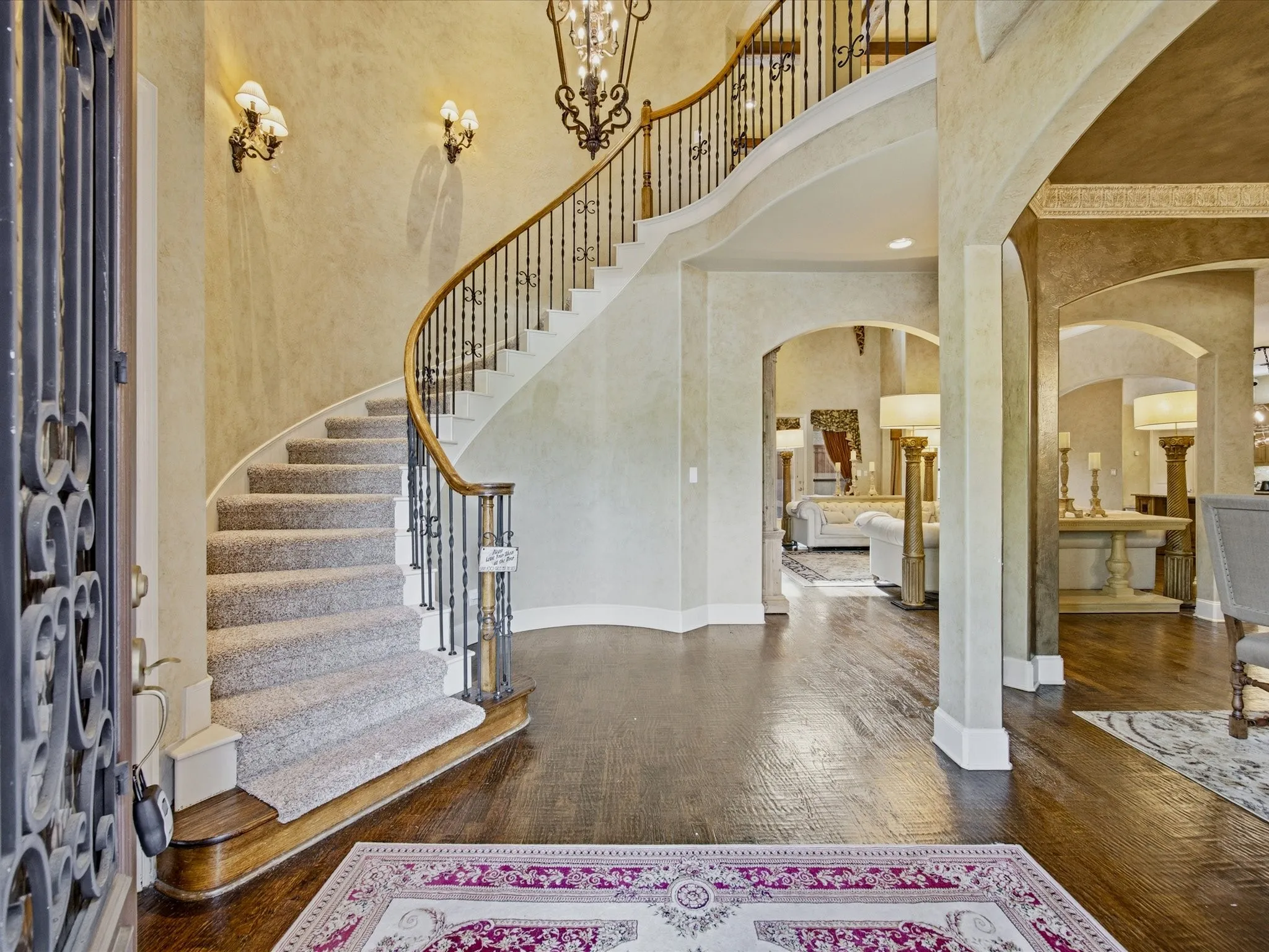 Grand entry featuring a curved staircase with wrought iron balusters and wood handrail, hardwood flooring, arched doorways, and textured wall finishes