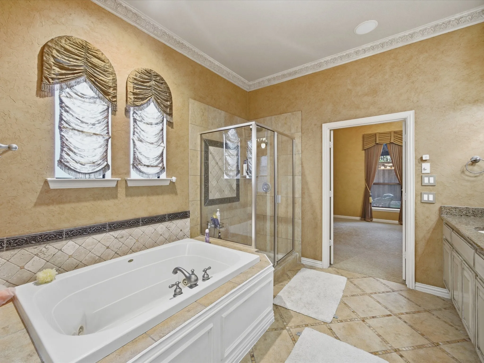 Soaking tub with tile surround, glass-enclosed shower, decorative wall tiling, and dual arched windows