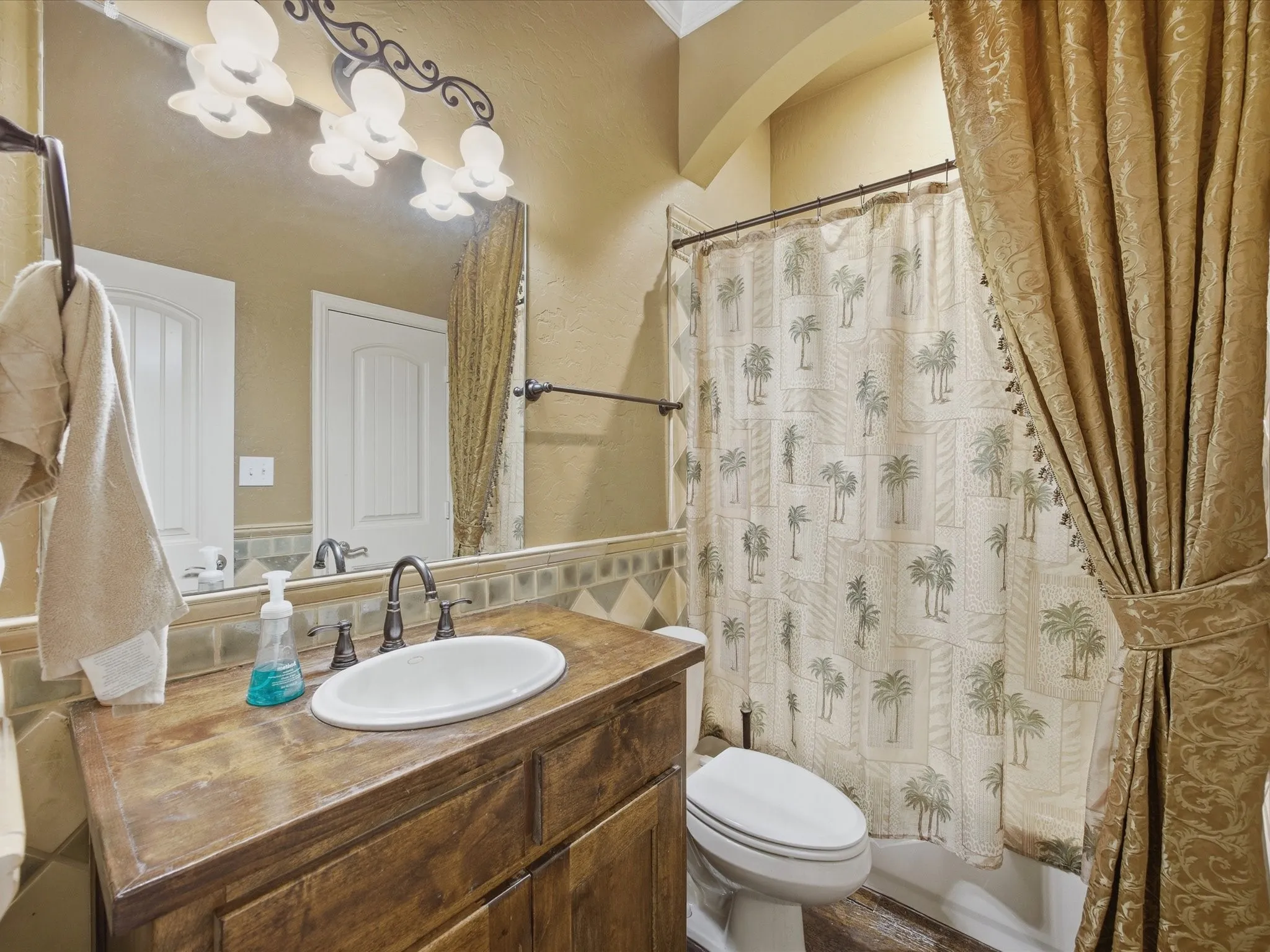 Wood-finish vanity with an oval basin sink, mosaic tile backsplash, and a three-bulb vanity light