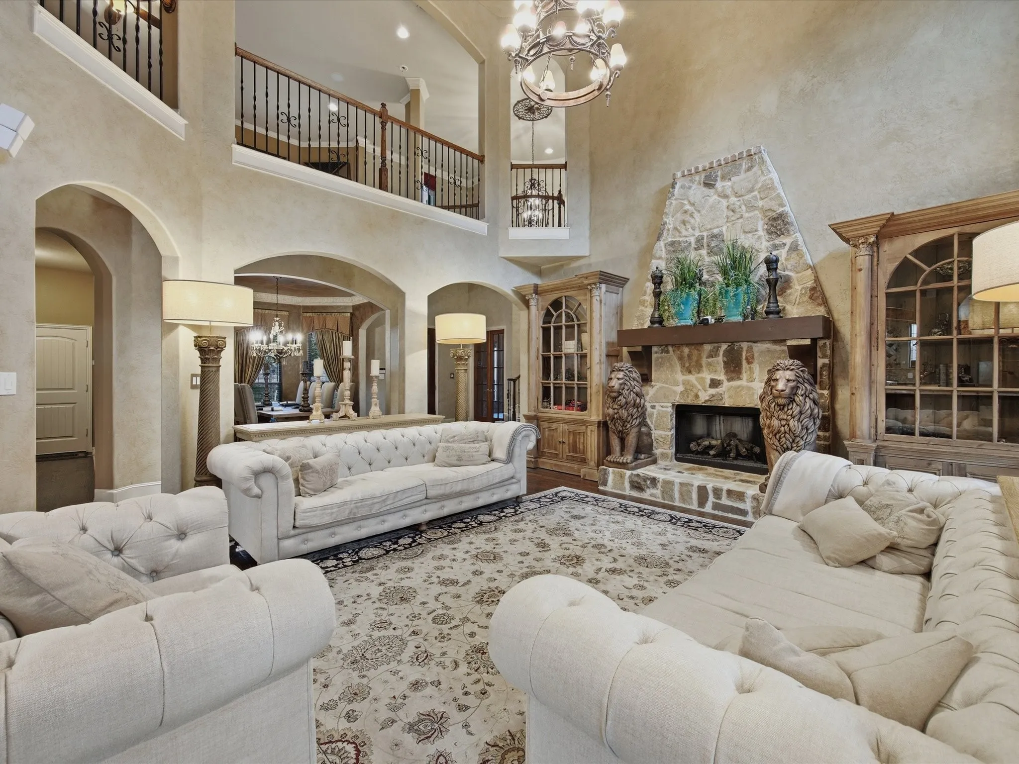 Two-story living area featuring a stone fireplace with a substantial wood mantel, arched doorways, and a second-story balcony with wrought iron railing
