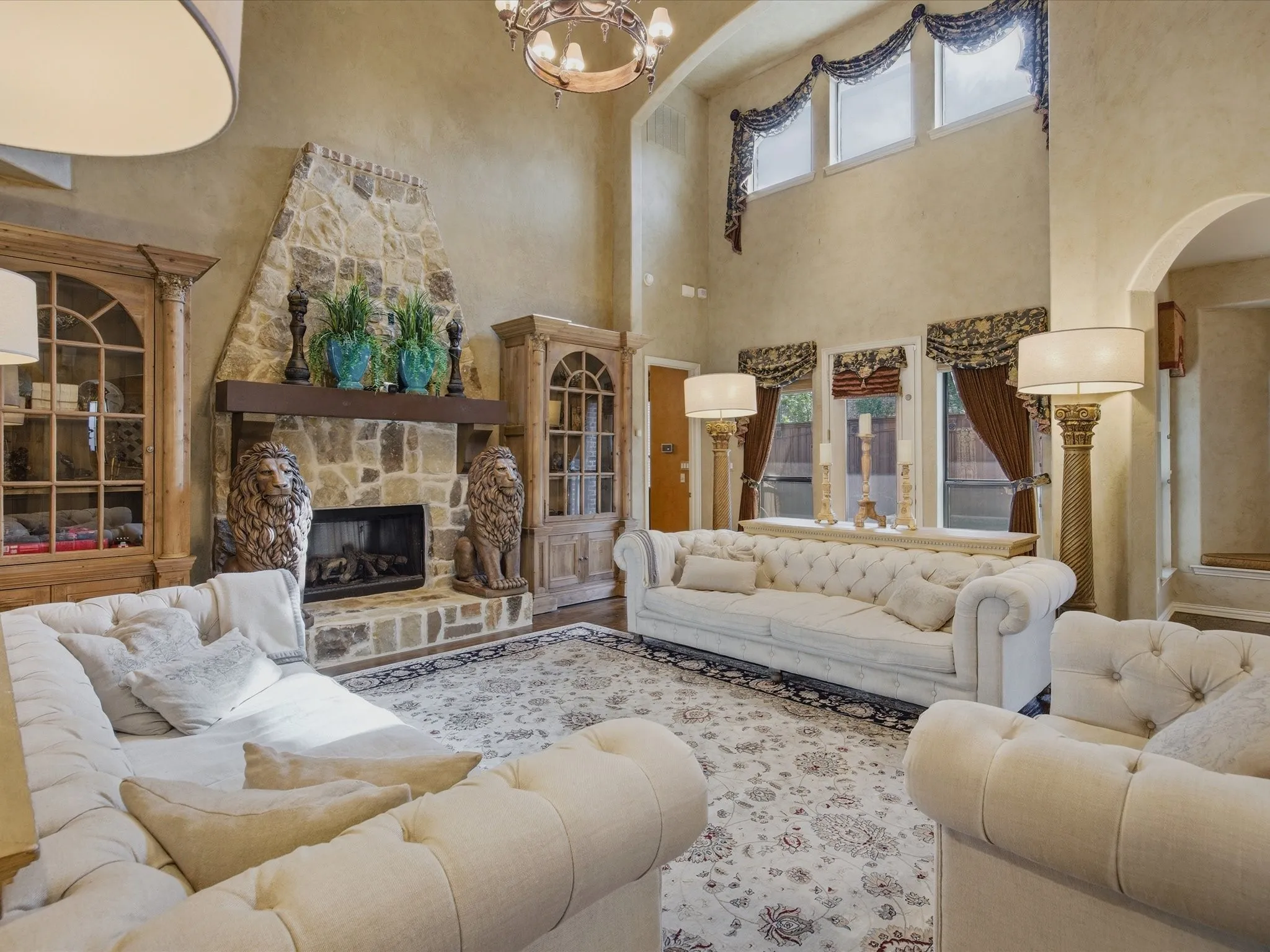 Stone-clad fireplace with mantel, arched entryway, high ceilings, multiple window configurations, and a chandelier