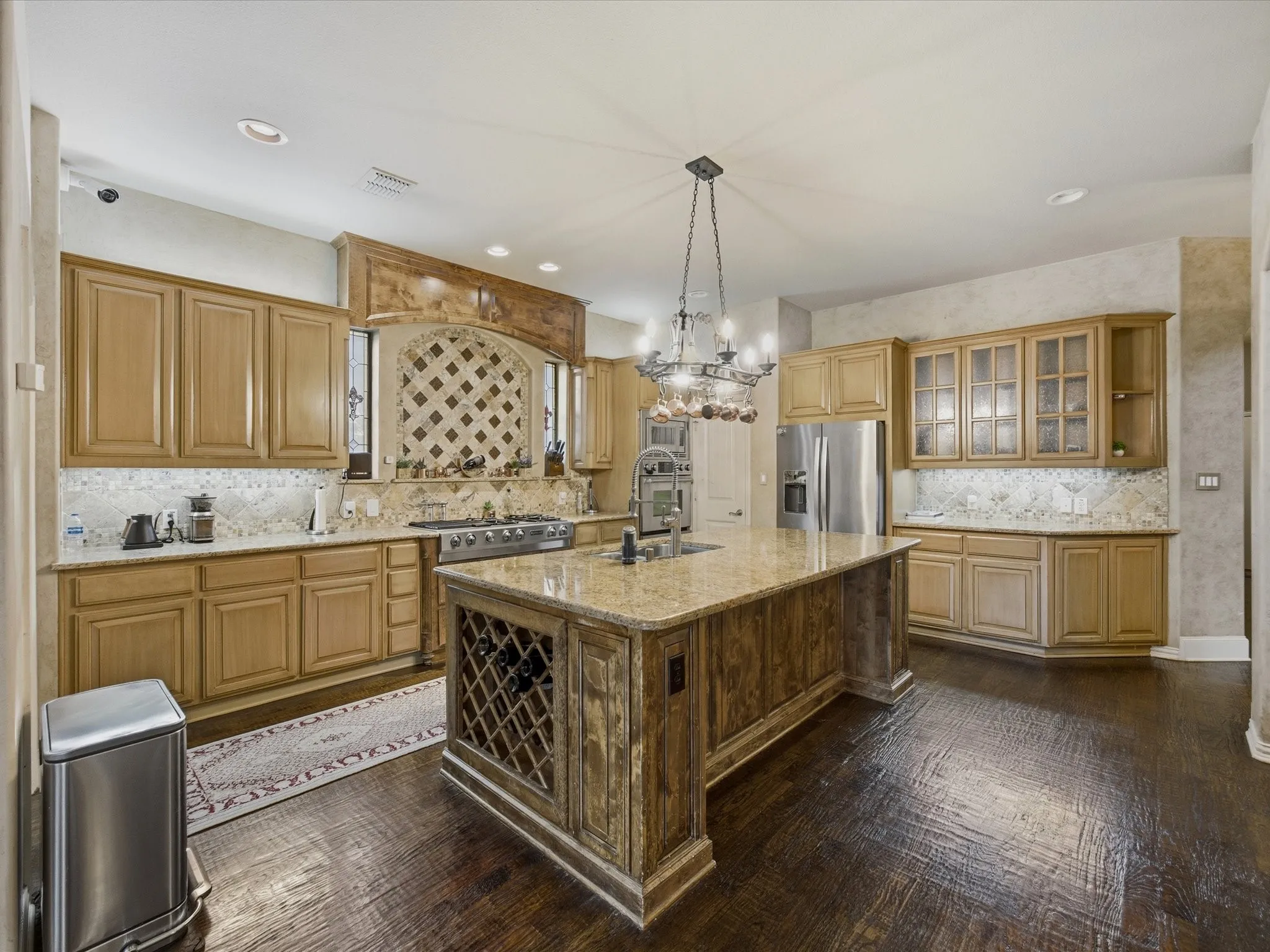 Kitchen featuring wood-finish flooring, custom cabinetry, a central island with integrated wine storage, granite countertops, and a tiled backsplash
