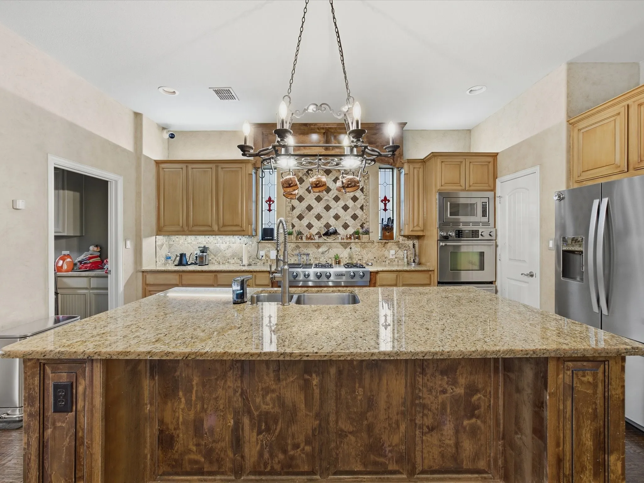 Kitchen featuring an expansive center island with a stone countertop, wood cabinetry, stainless steel appliances, and a decorative pot rack with integrated lighting