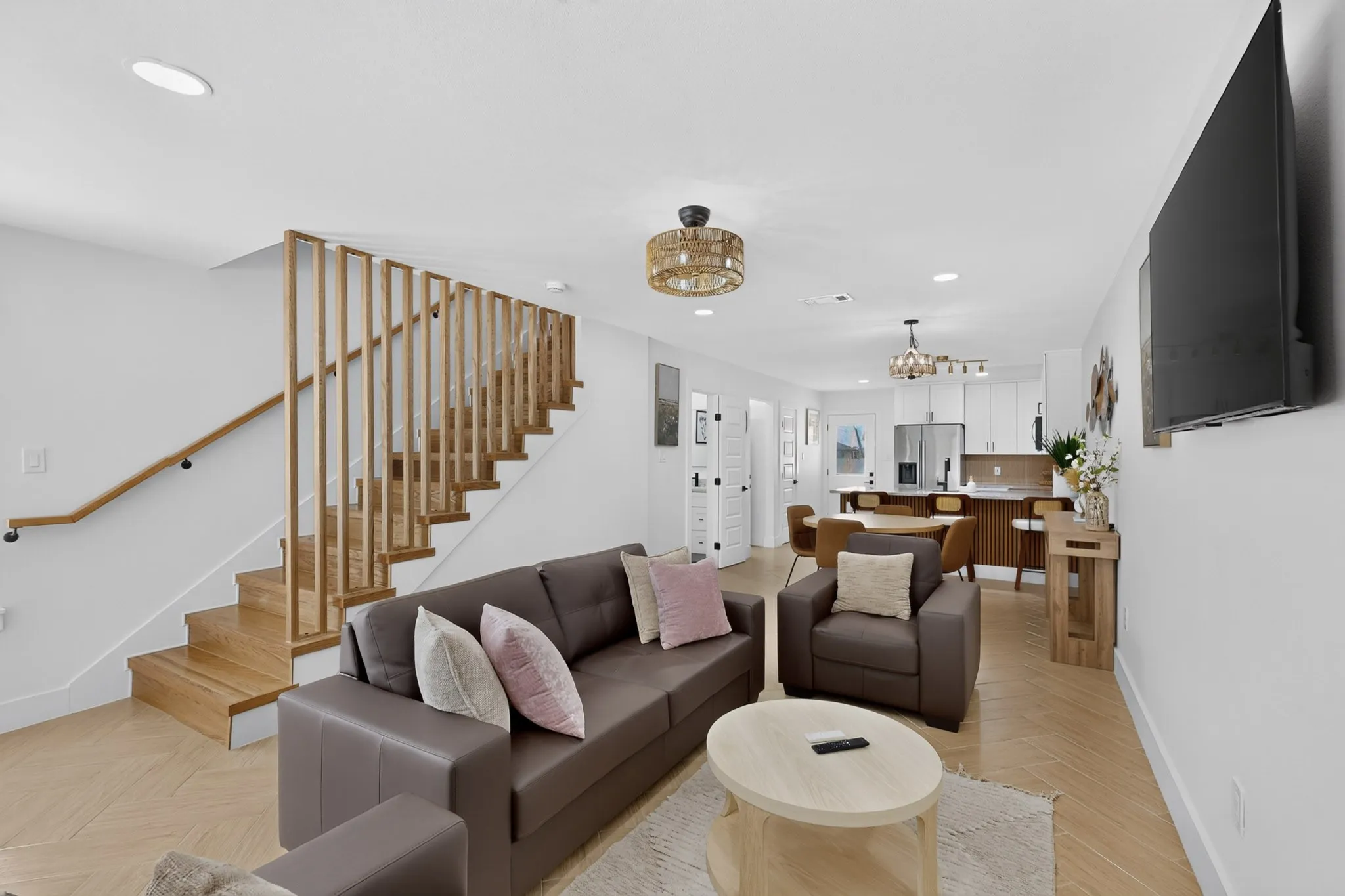 Open-concept living space featuring wood-finish flooring, a contemporary wood slat staircase, recessed lighting, and a modern kitchen with a center island