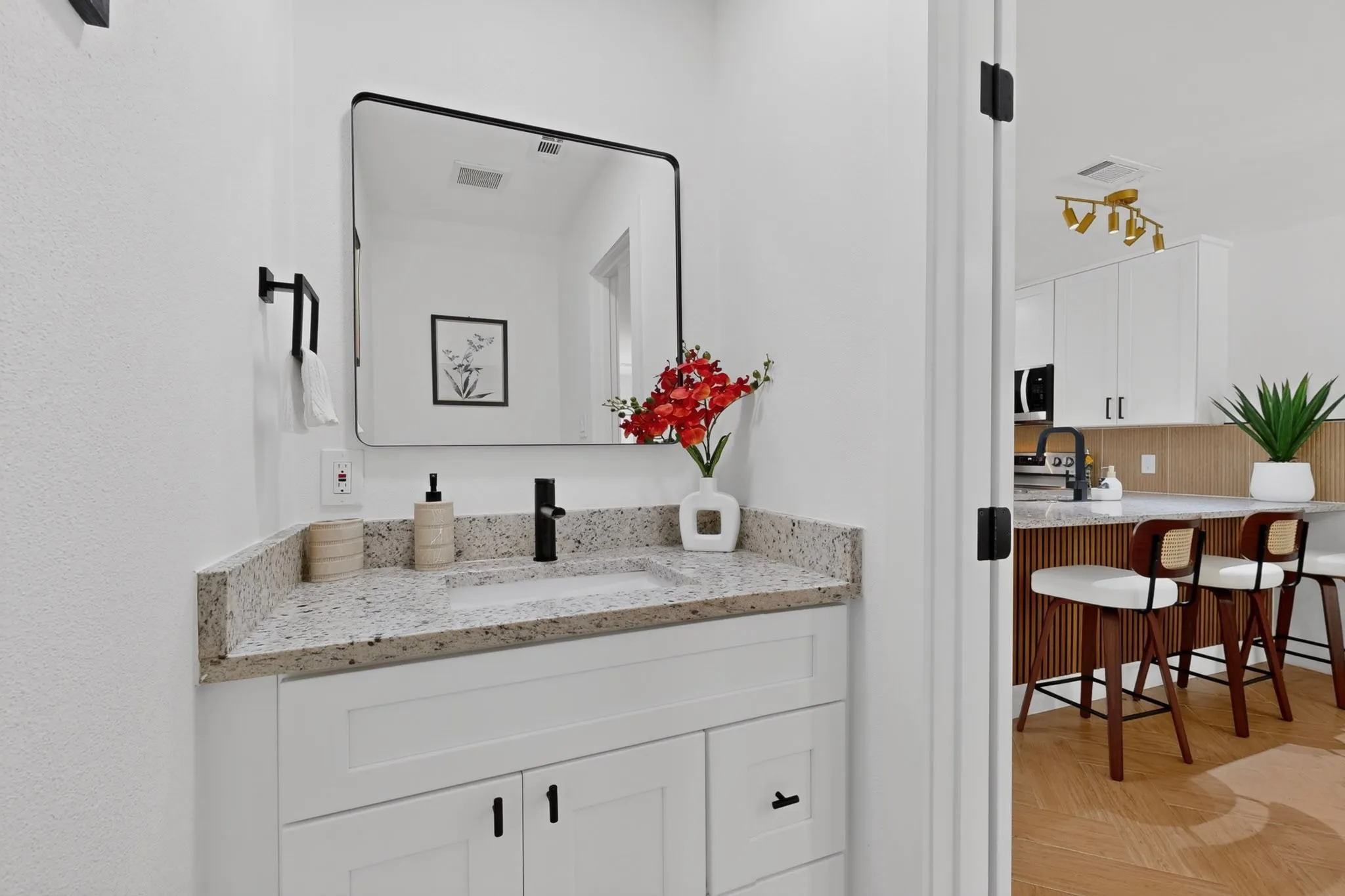 White vanity with black hardware, granite-style countertop, and a black-framed mirror